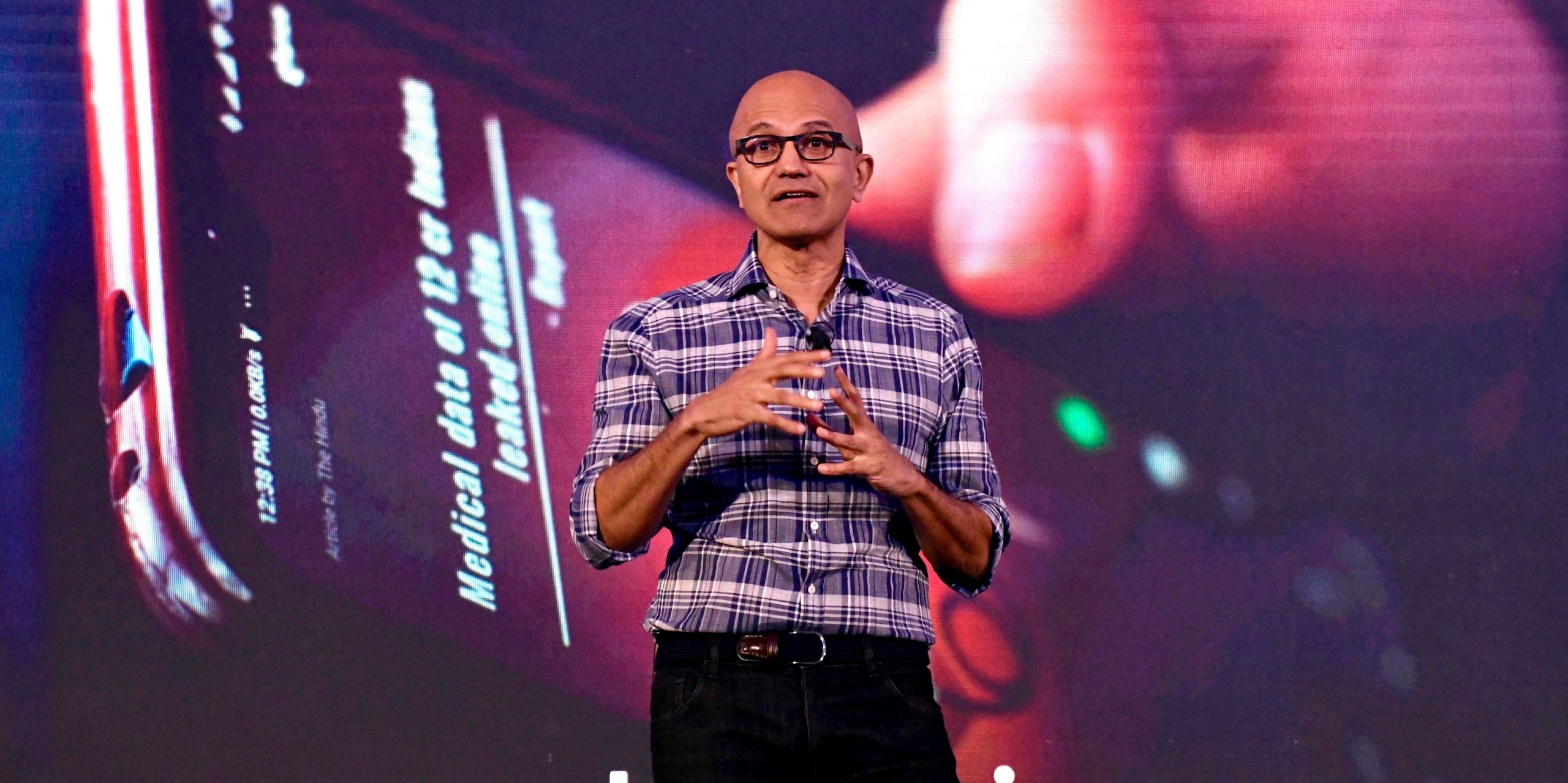 Satya Nadella speaks in front of the image of a cell phone.