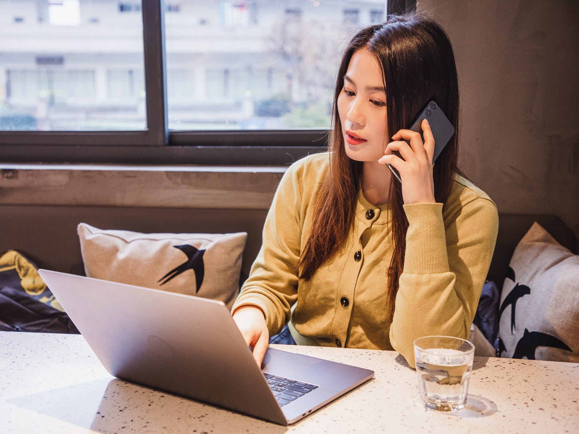 Woman in a yellow sweater talking on her phone in front of a computer