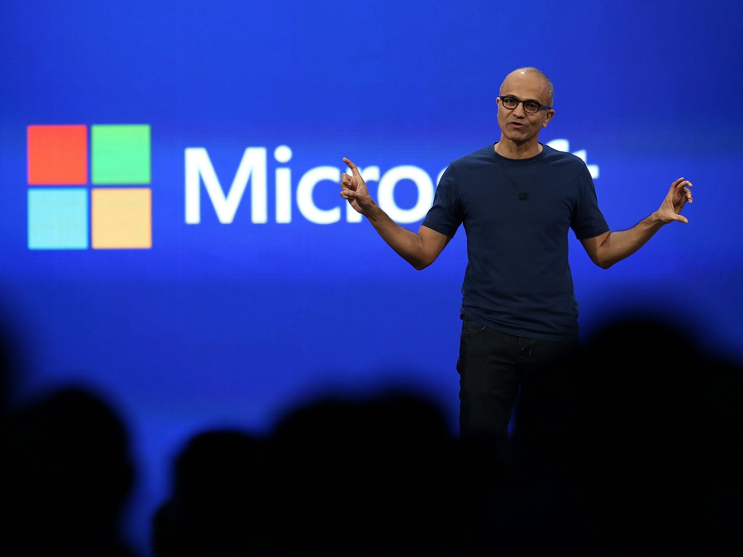 Microsoft CEO Satya Nadella stands on stage and gestures widely with both hands