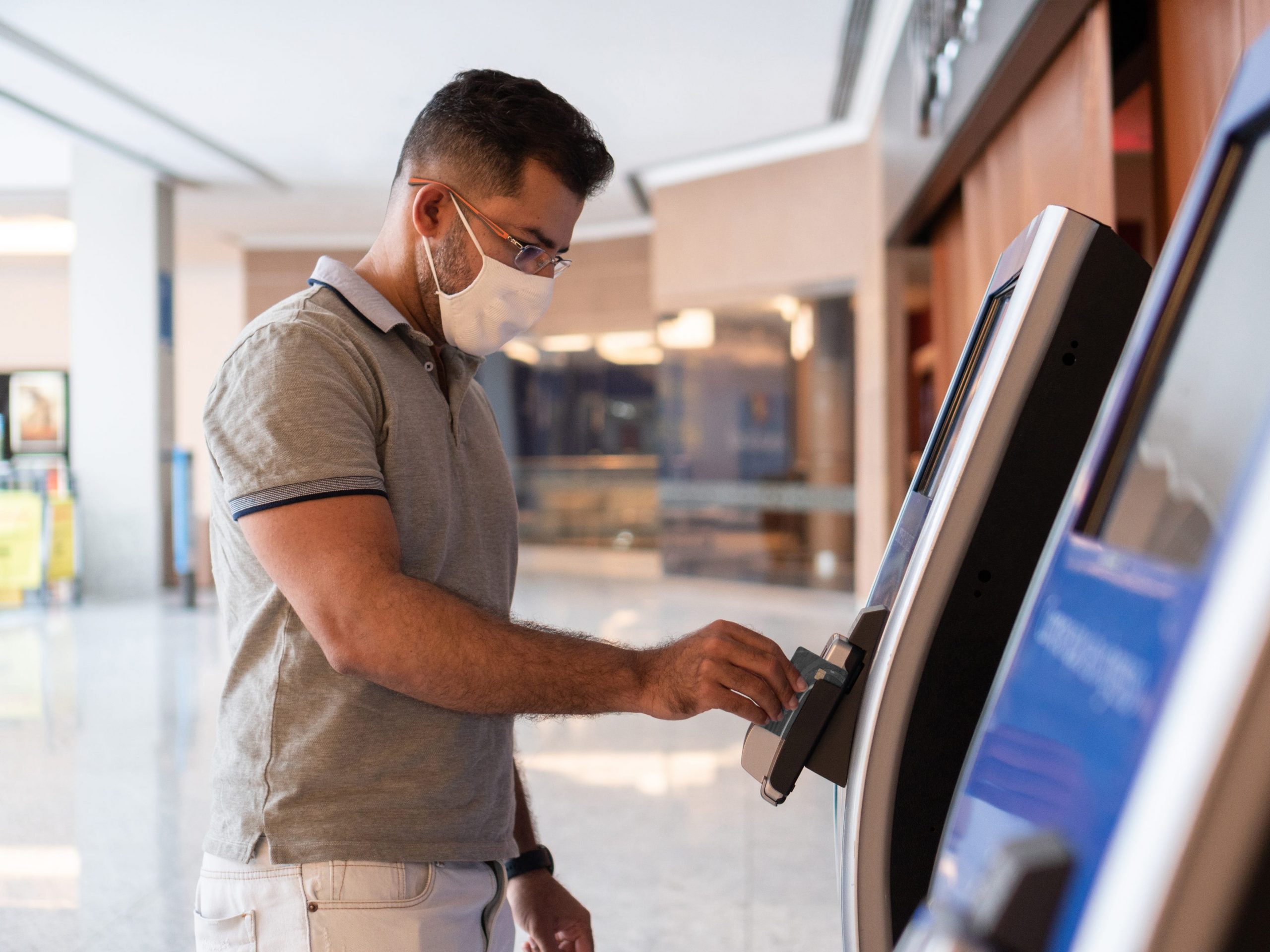 Man wearing mask inserting bank card into ATM.