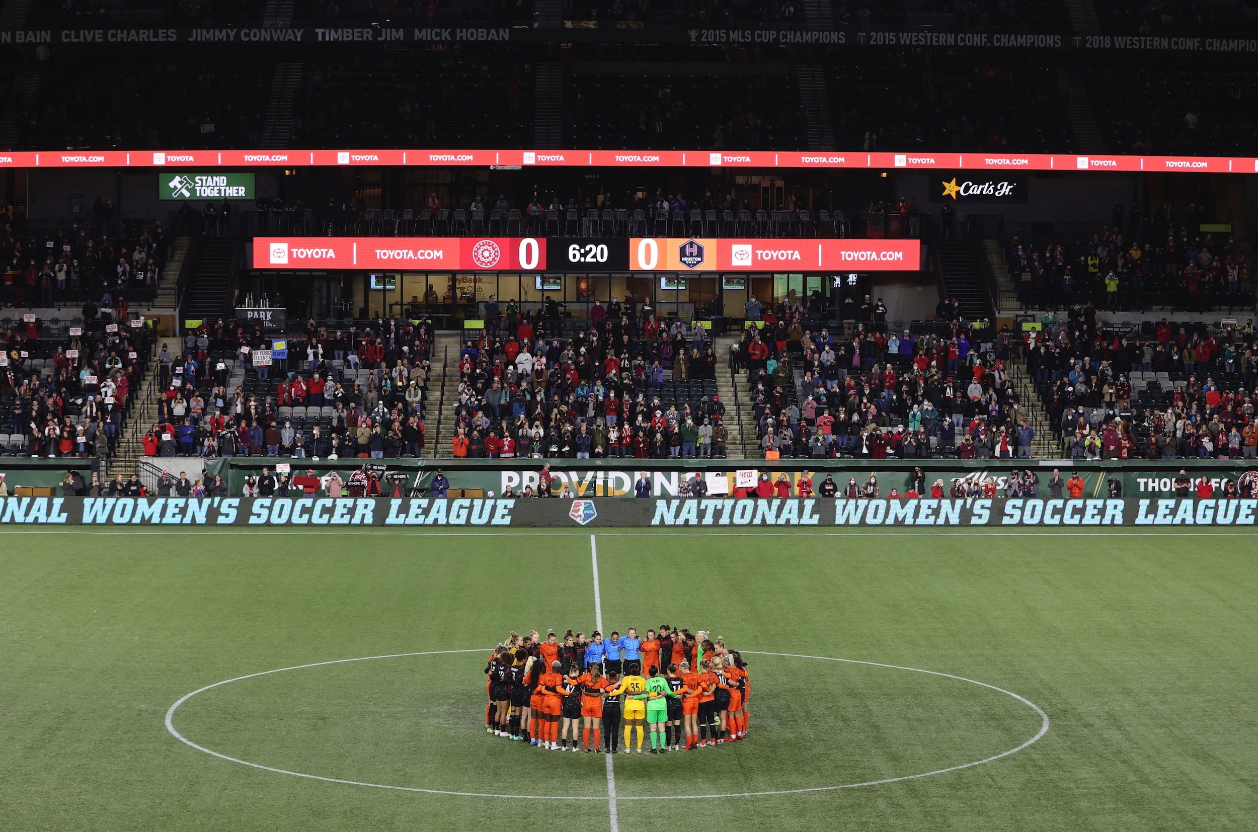 NWSL players from the Portland Thorns and Houston Dash pause their game and huddle in the center circle to protest the league and honor survivors of sexual abuse at the hands of a former coach.