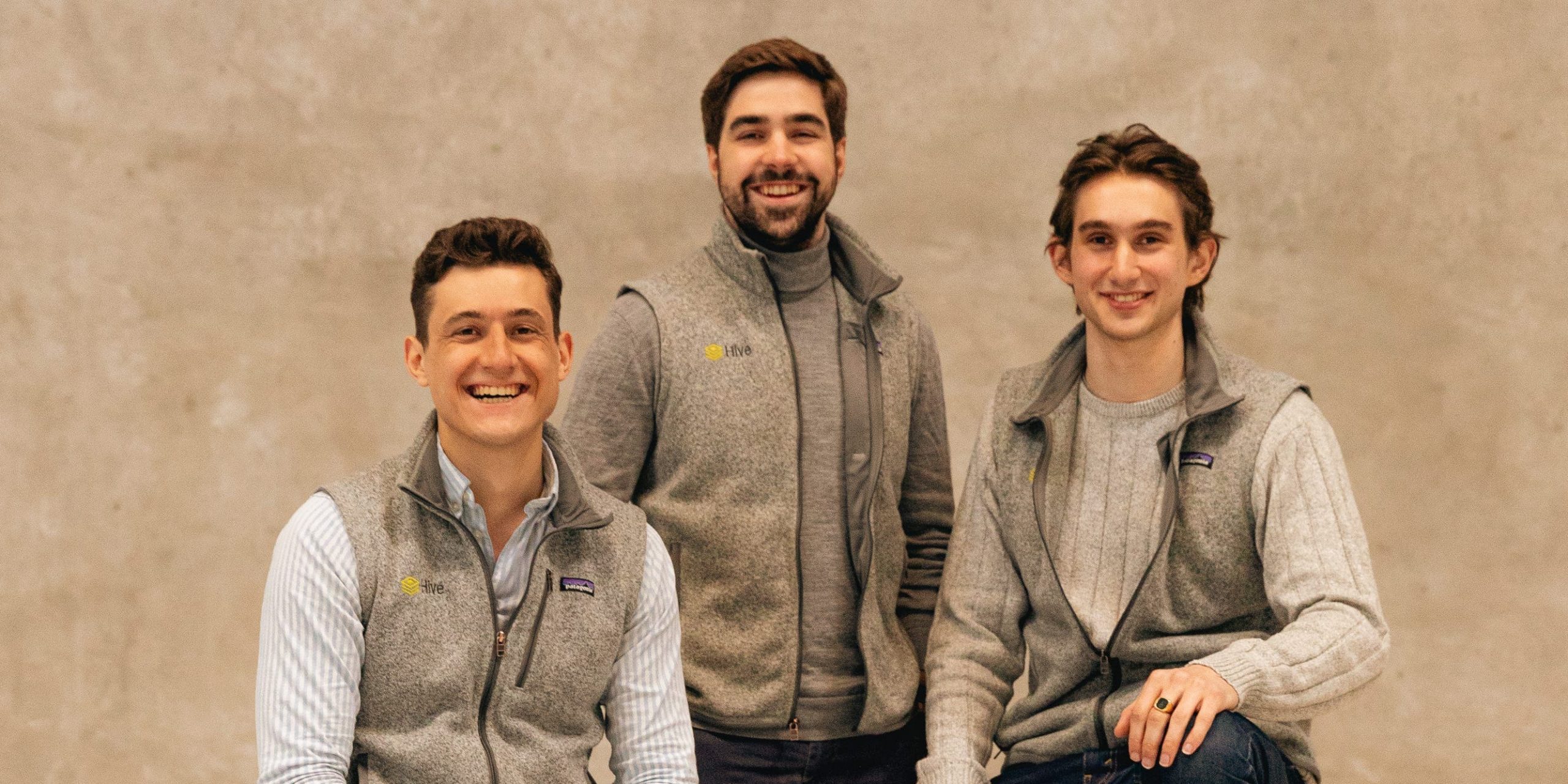 Hive cofounders, wearing grey vests, posing against boxes and wooden pallets