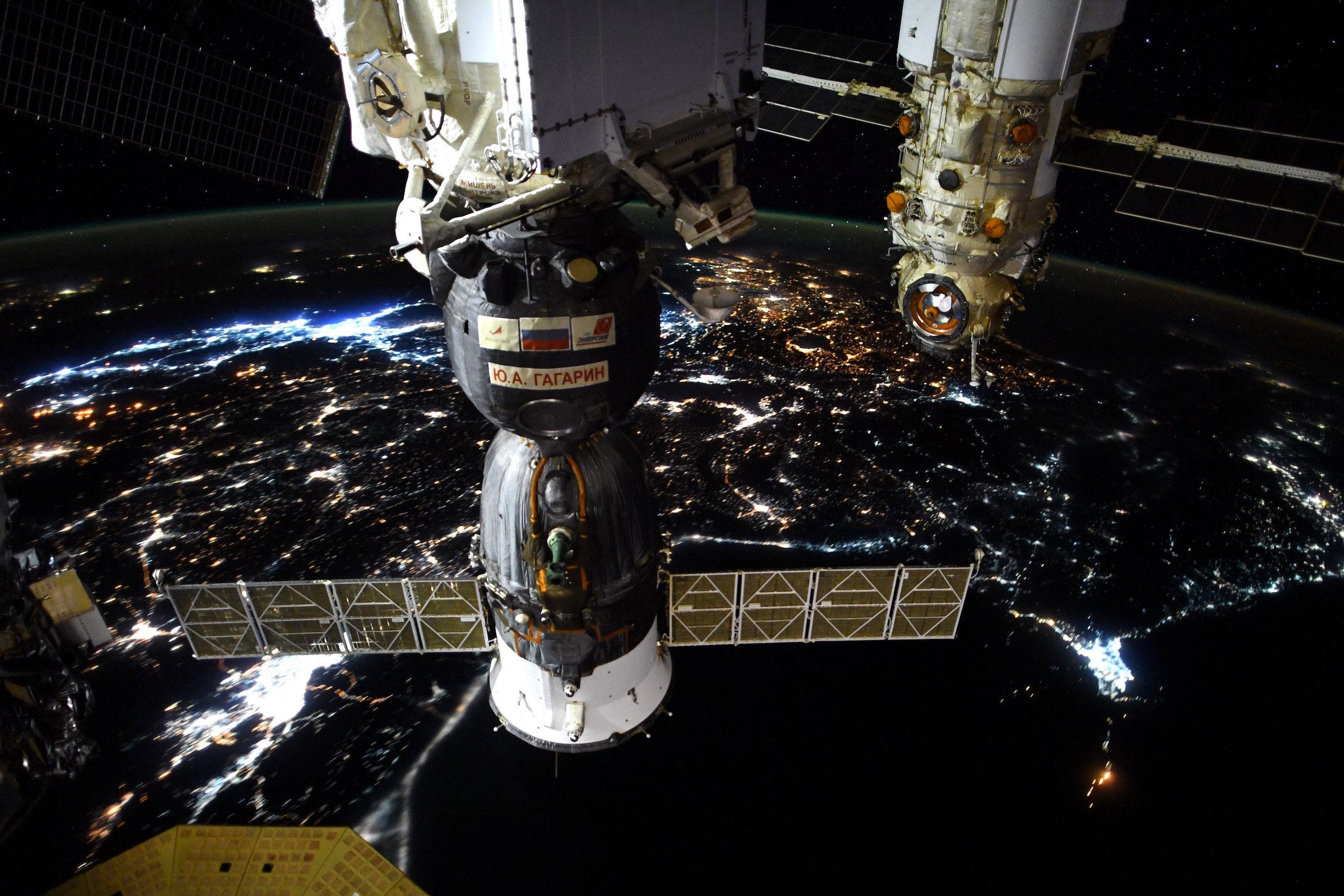 spaceships docked to the space station above nighttime earth