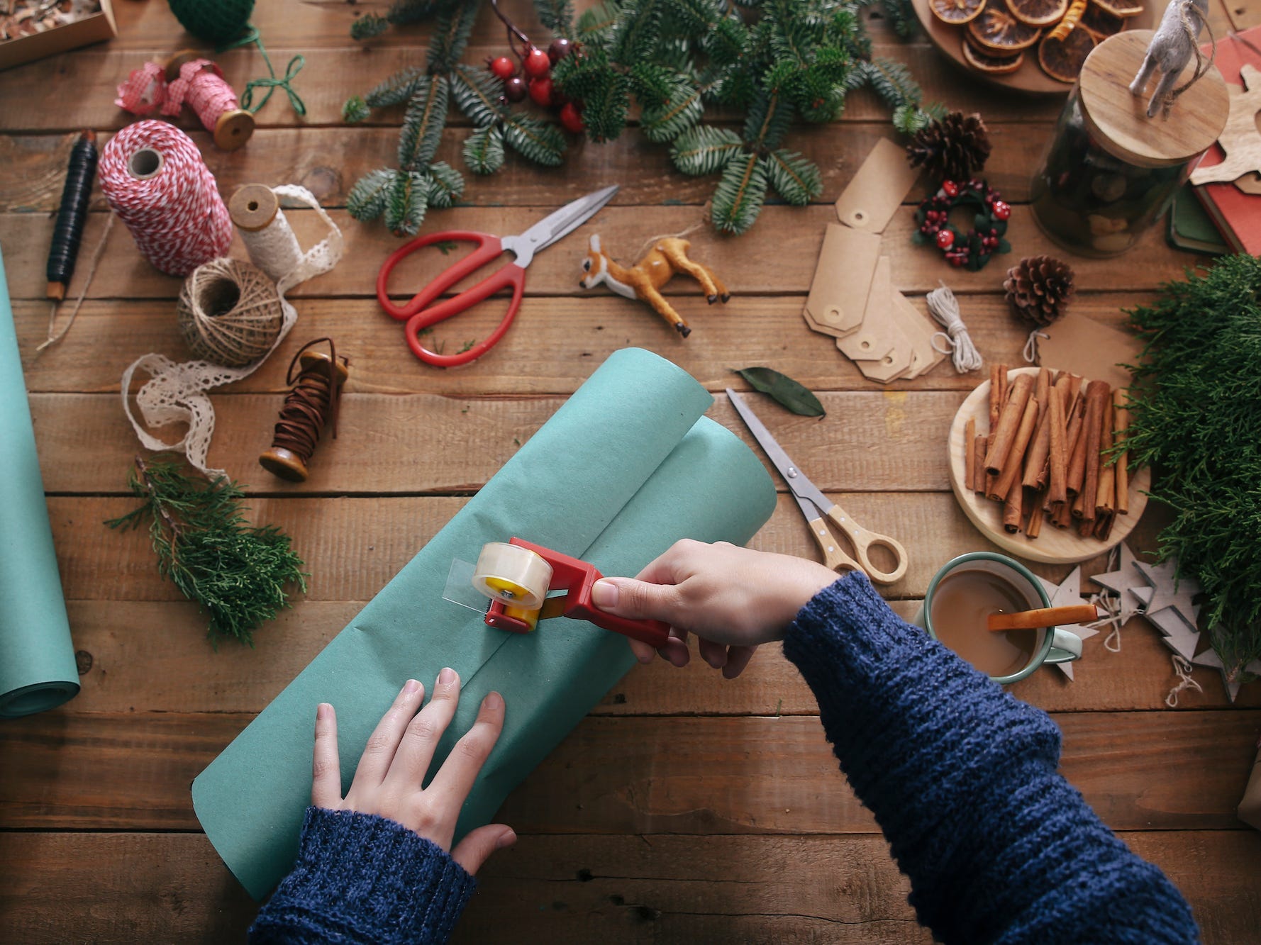 A person wraps a present on a table full of gift wrapping supplies.