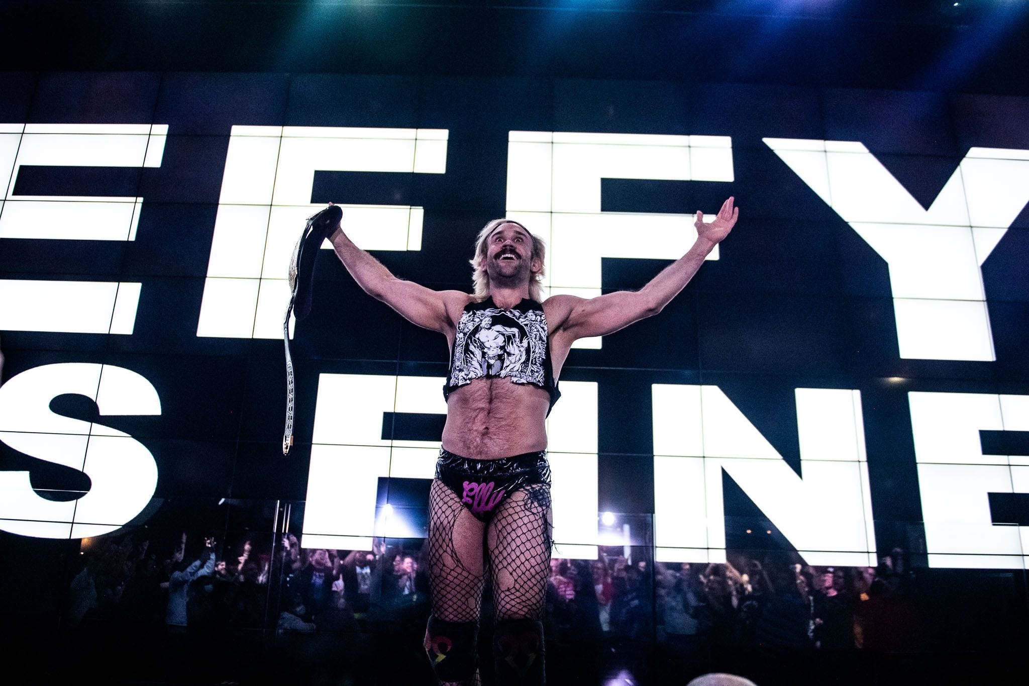 Independent wrestler Taylor Gibson, who goes by EFFY, standing in front of a large lighted sign with his name on it.