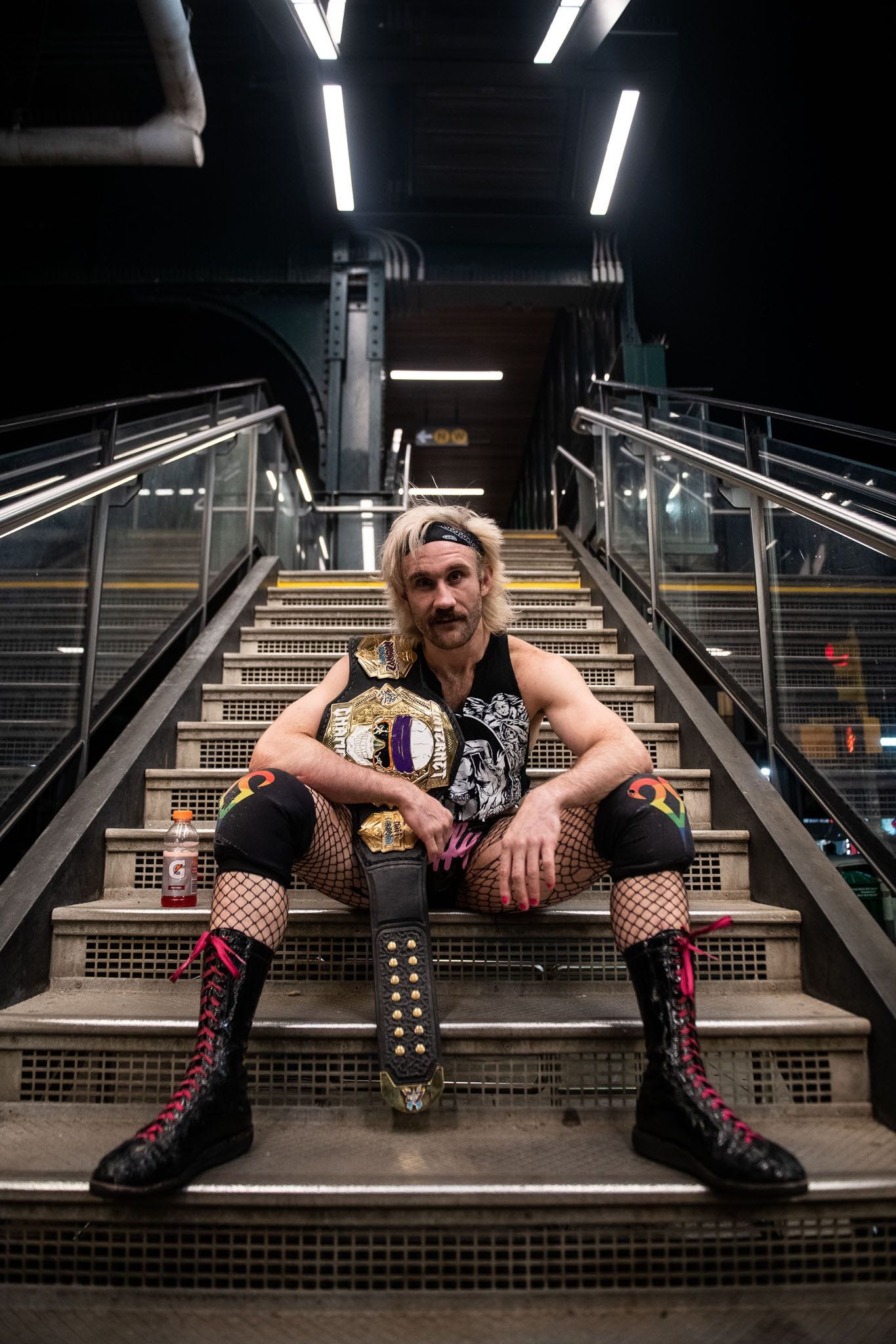 Independent wrestler Taylor Gibson, who goes by EFFY, siting on a set of stairs with a championship belt.