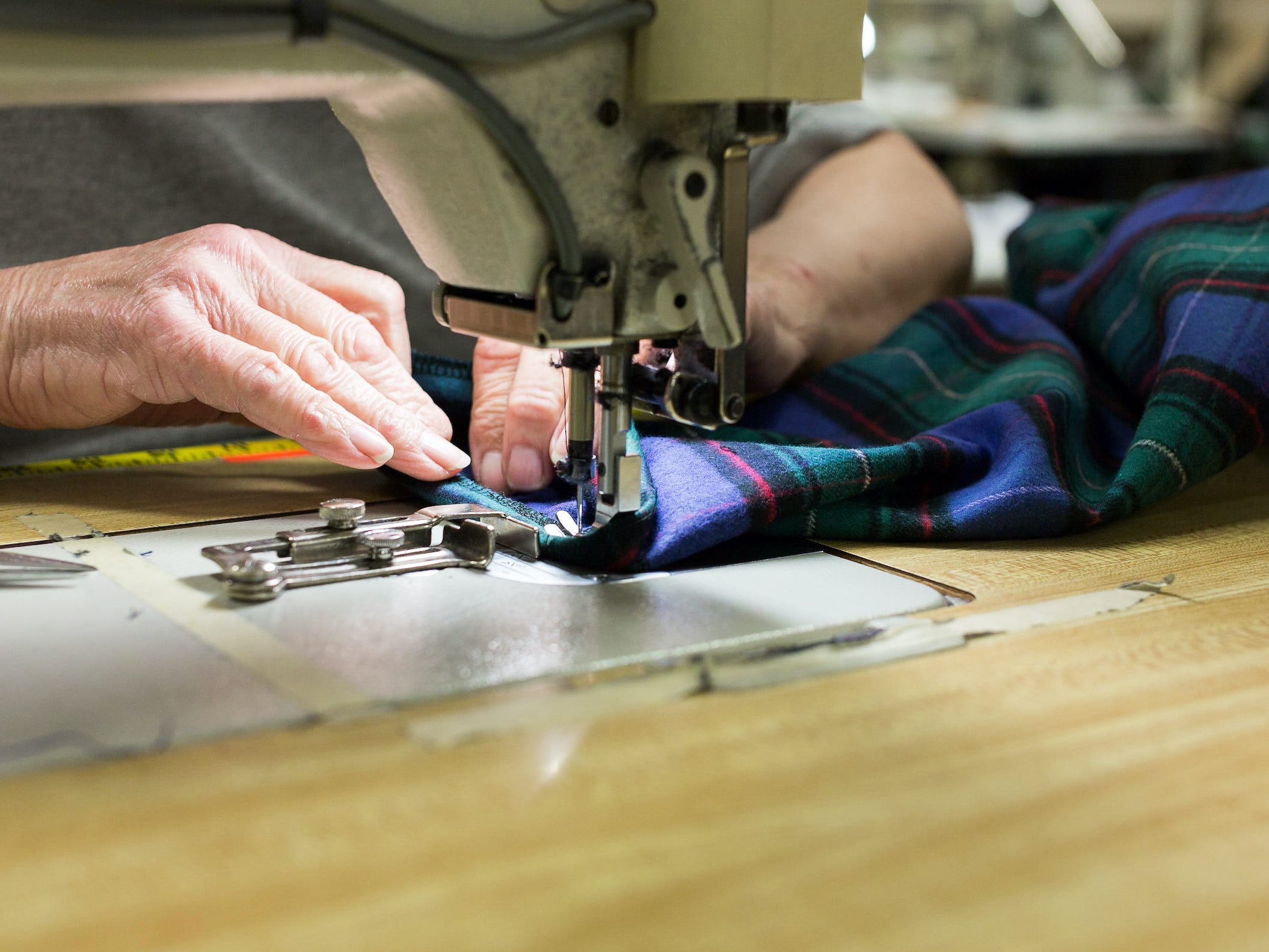 Person holds flannel fabric under sewing machine at Vermont Flannel Company facility