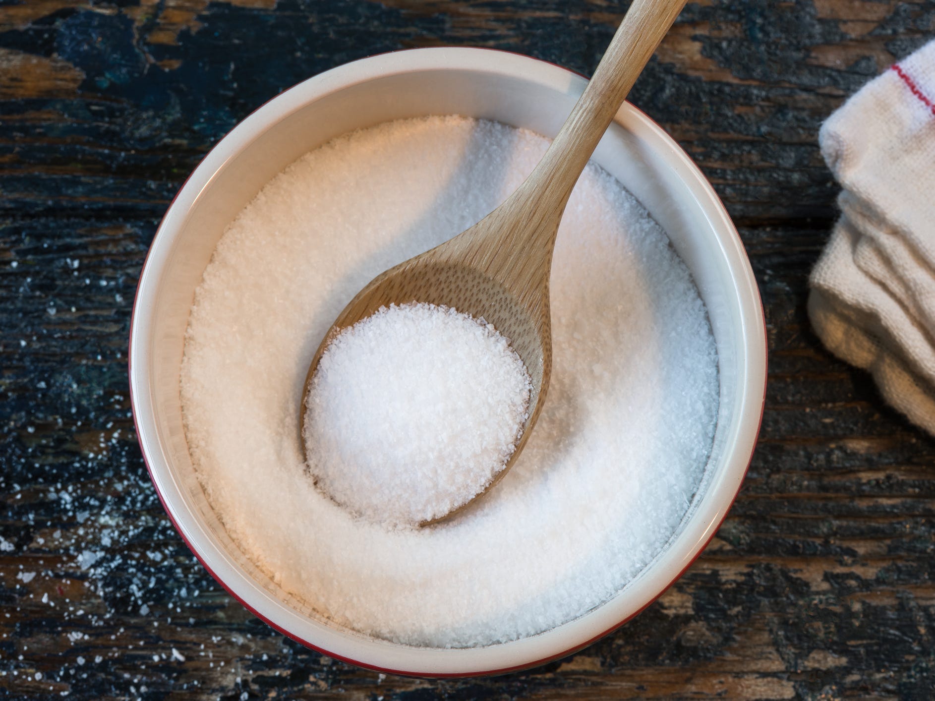 A bowl of kosher salt with a wooden spoon in it viewed from above