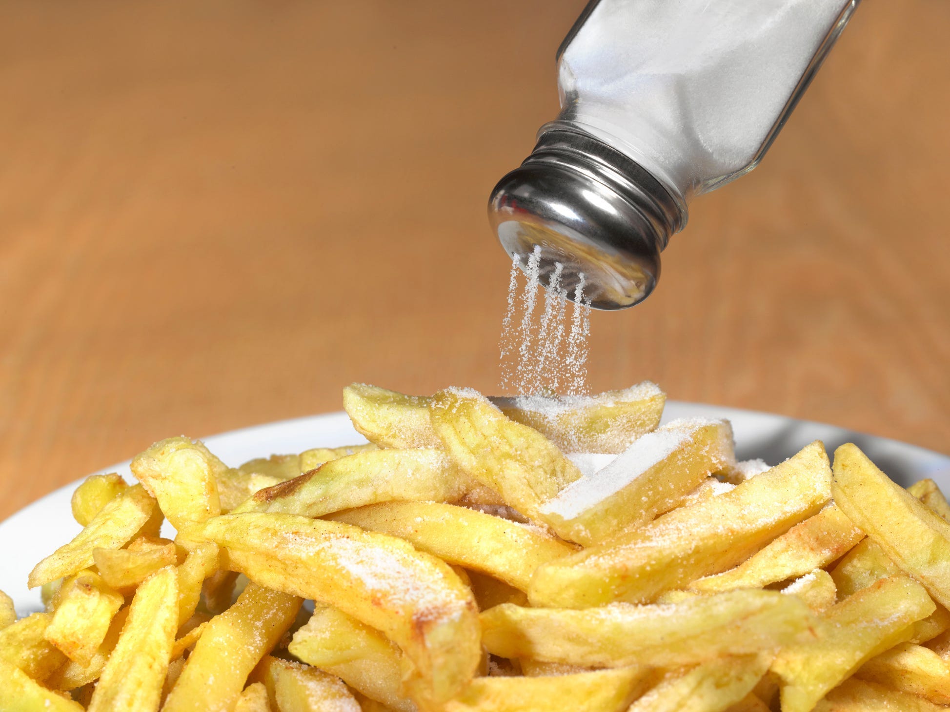 A salt shaker turned upside down dumping too much salt onto a plate of french fries