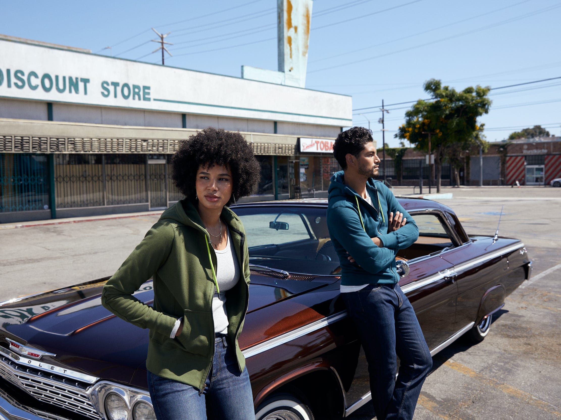 Woman and man lean against classic car wearing American Giant hoodies