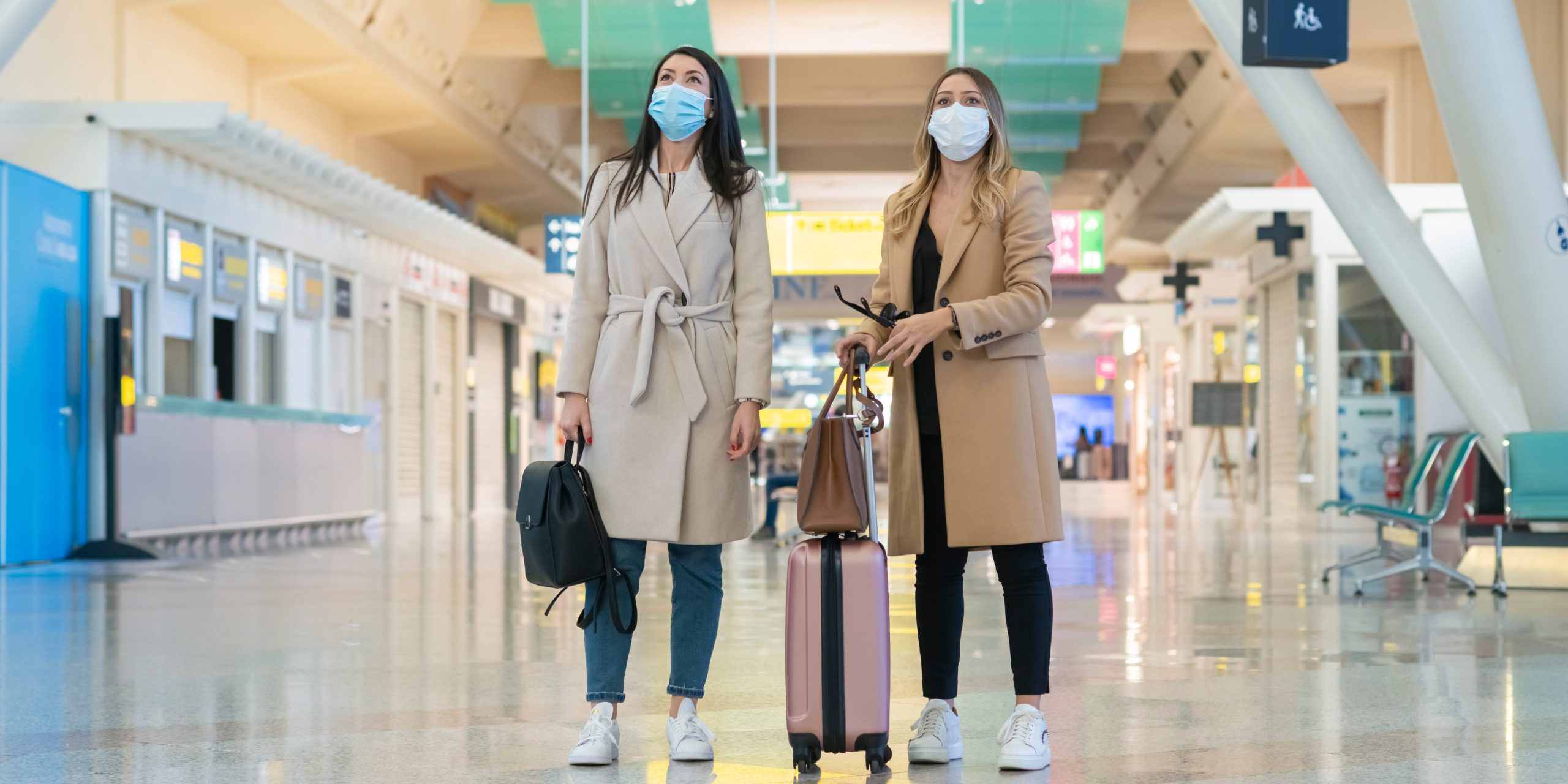 Two young women wearing masks while waiting together in an airport