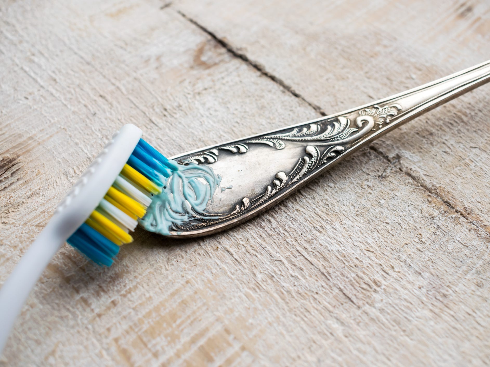A toothbrush scrubbing toothpaste onto the ornate handle of a silver utensil