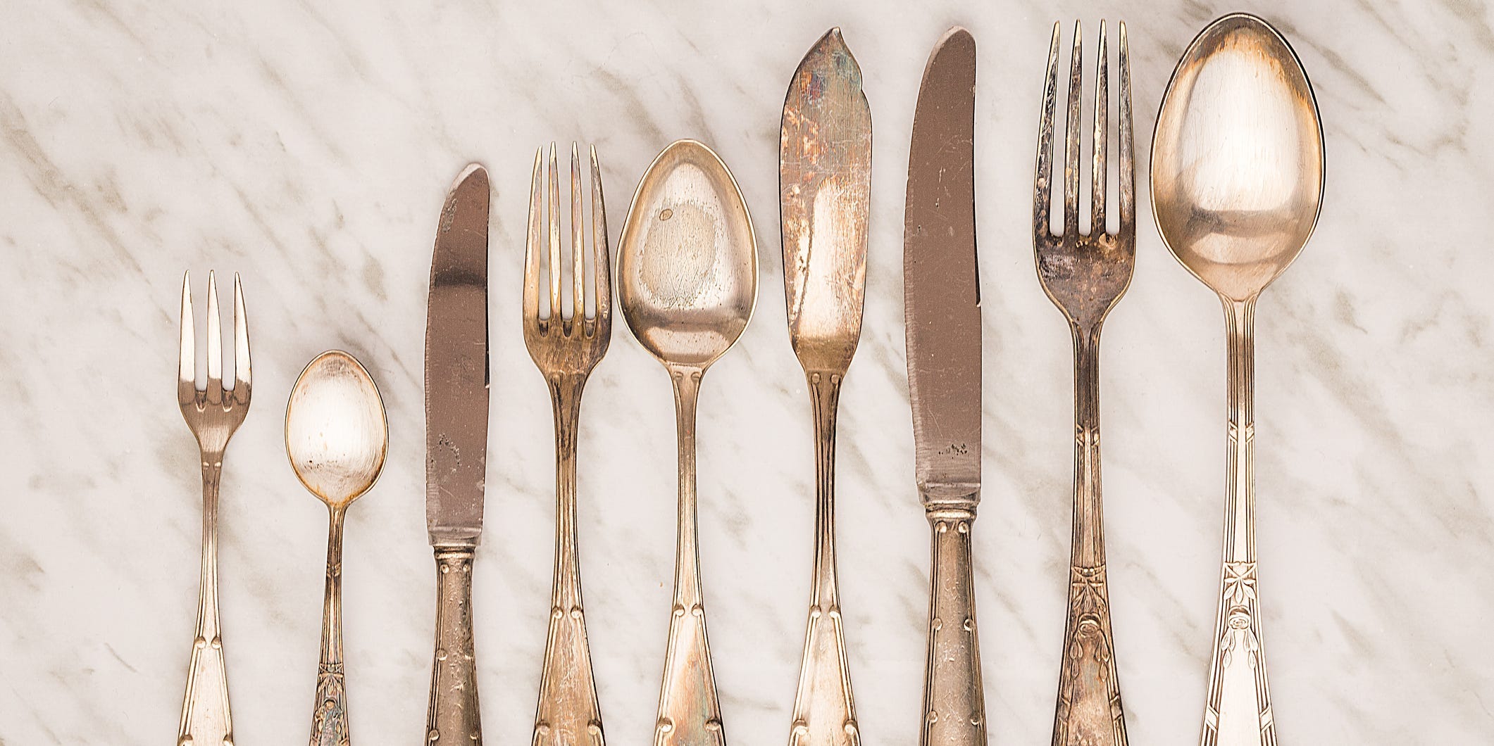 Several tarnished silver forks, knives, and spoons lined up in size order
