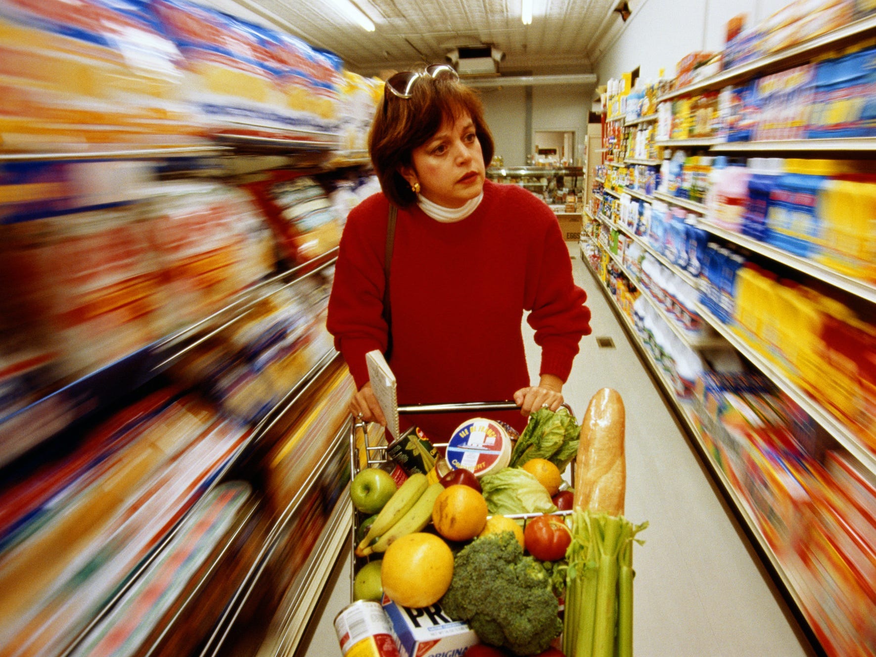 Woman pushing shopping cart filled with food in a supermarket aisle