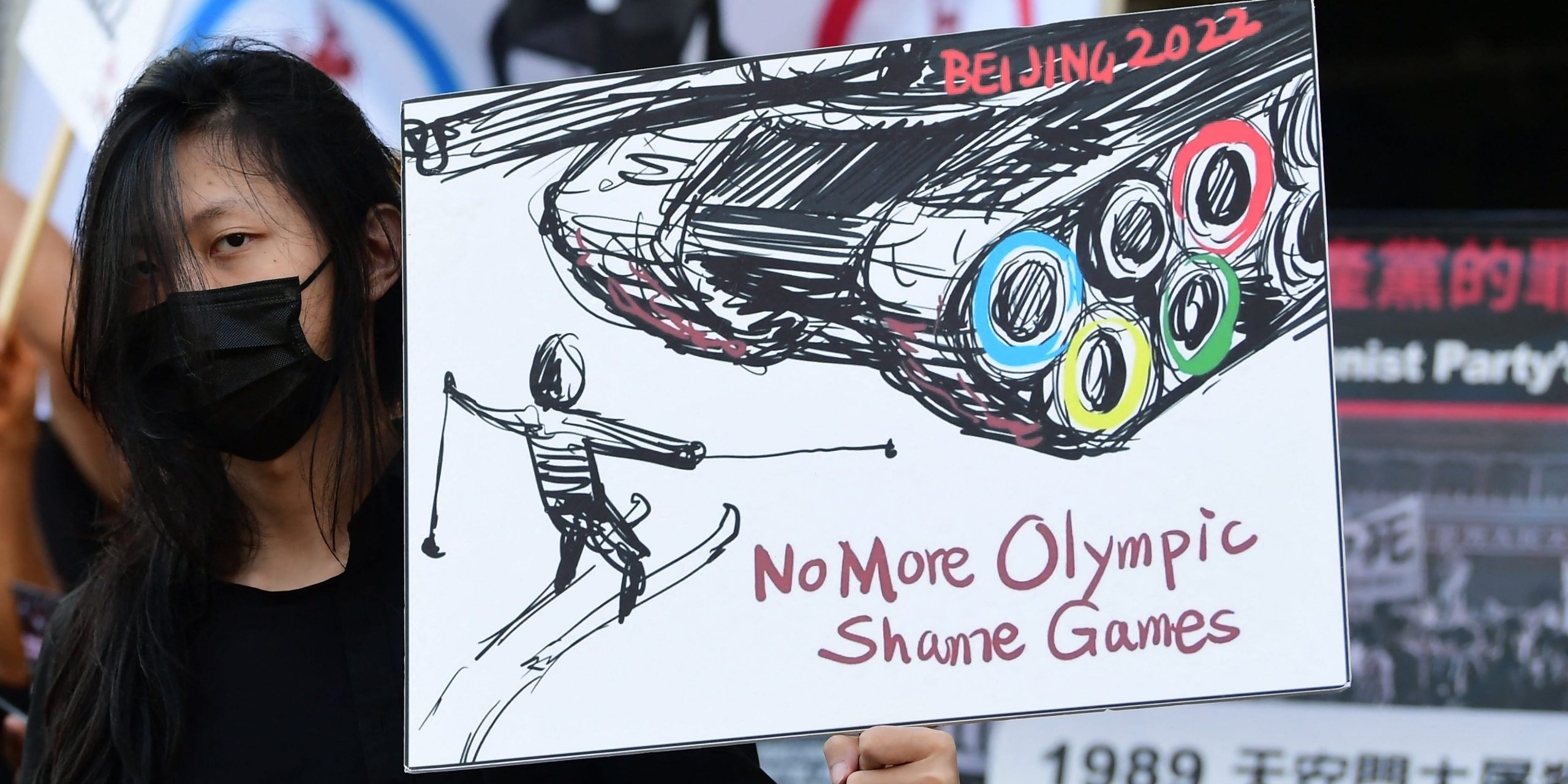 A woman in a black mask protesting China hosting the Olympics holds a sign picturing a tank with Olympic rings confronting a man in skis.