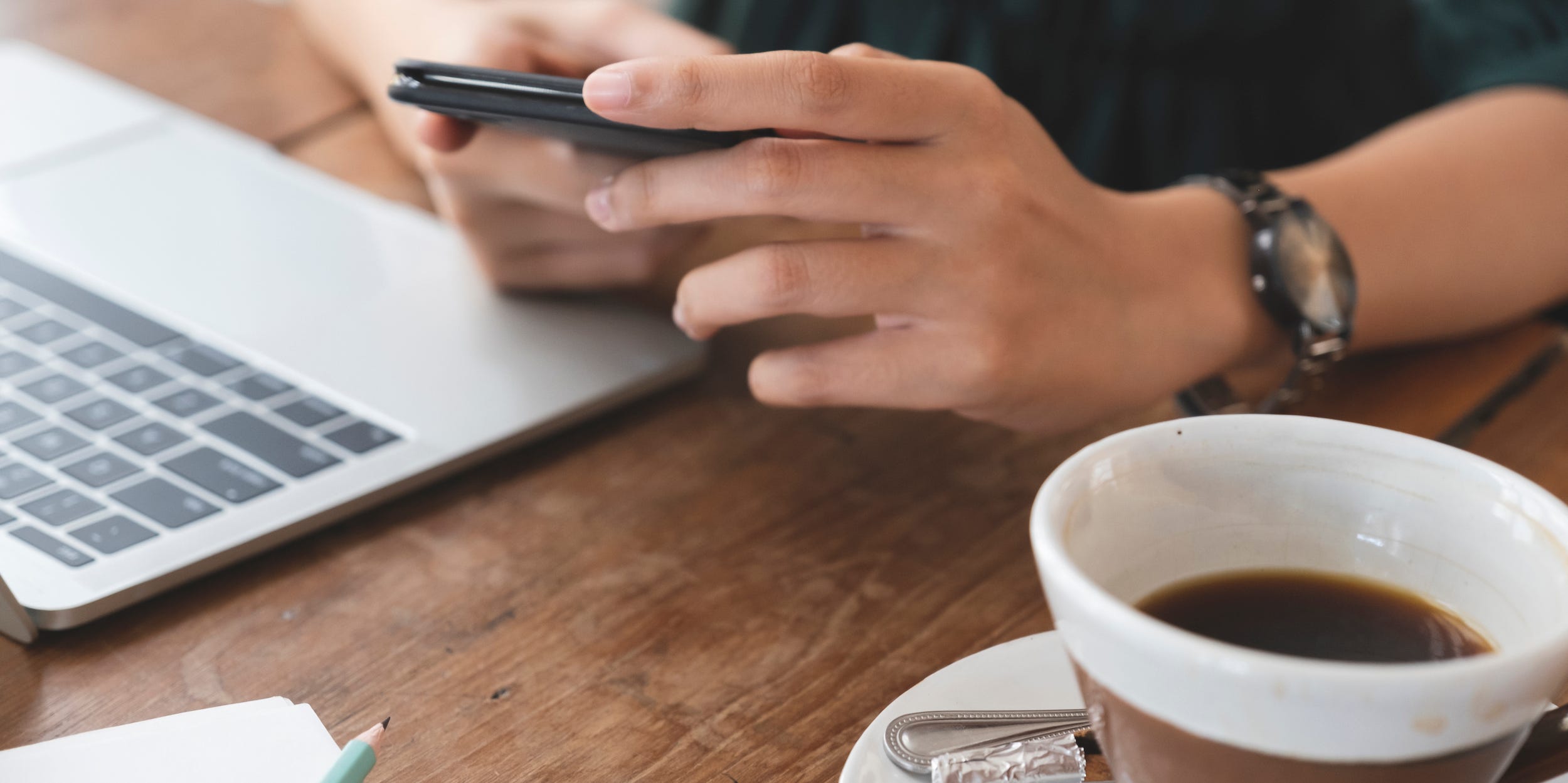 person at desk using phone and laptop with coffee cup