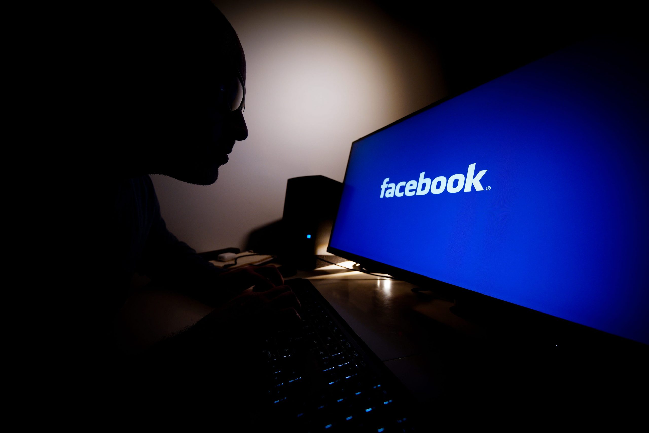 A man looks at a computer screen with the Facebook logo