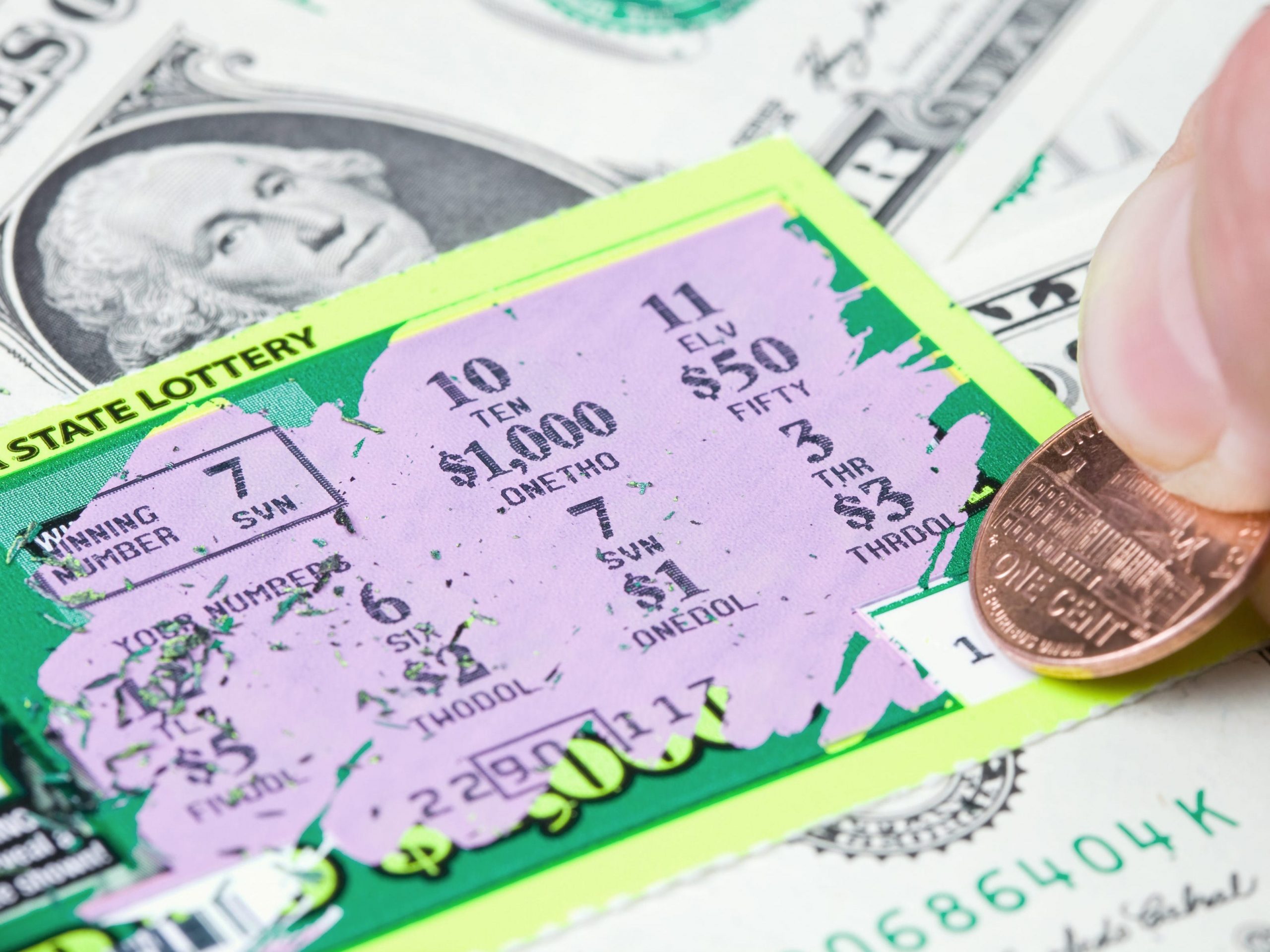 A lottery player scratching a winning ticket which rests on a dollar bill background.