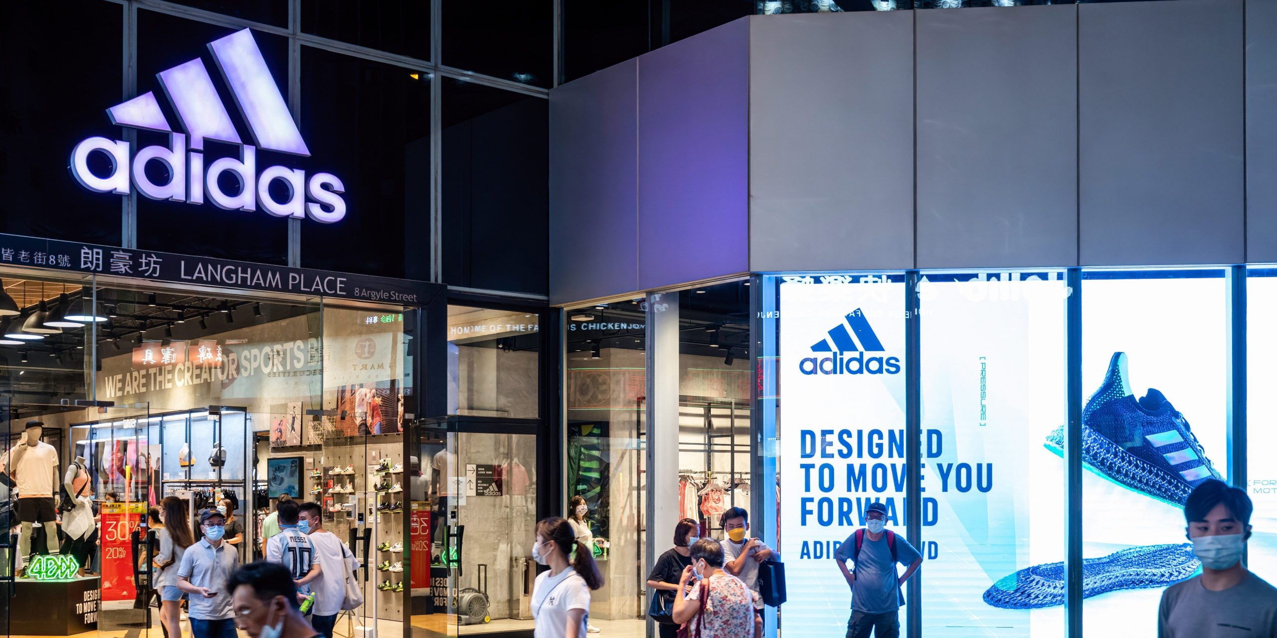 Pedestrians walk past the German multinational sportswear brand Adidas store and logo in Hong Kong.