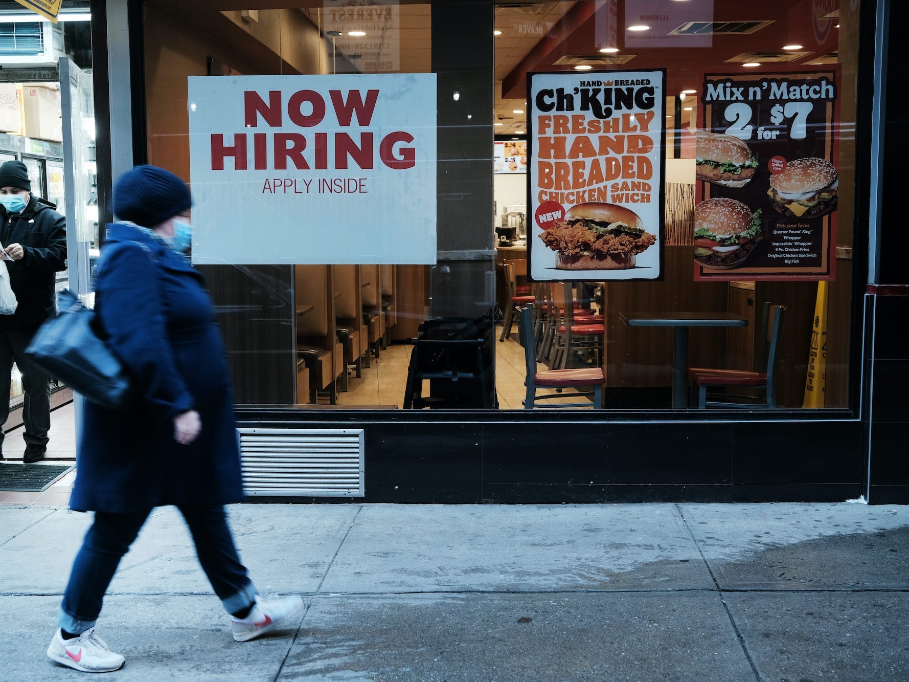 A person walks by a sign advertising employment at a fast-food restaurant