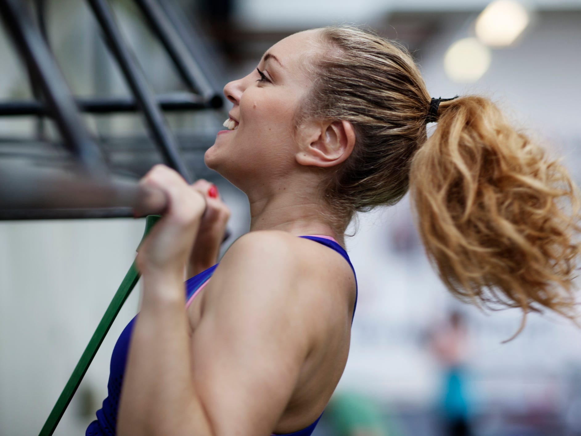 An athlete with a ponytail hanging from a bar at the top of a pull-up exercise