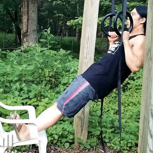 an athlete doing feet-assisted pull-ups outdoors with a chair
