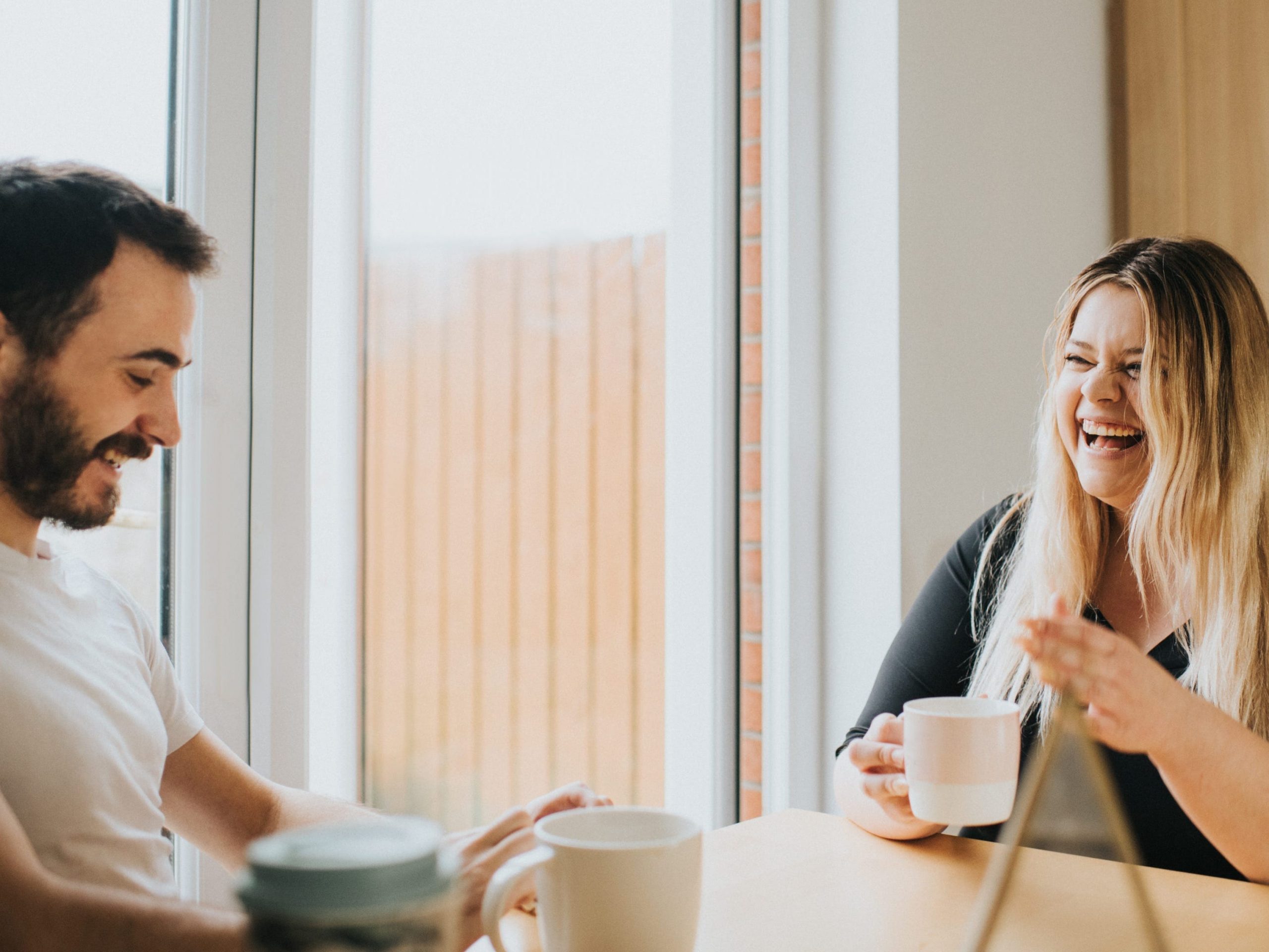 Couple sit at a Dining Table and enjoy hot drinks, while chatting with each other