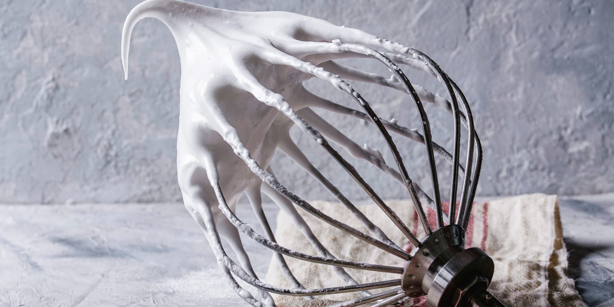 The whisk of a stand mixer laying on the counter with a perfectly peaked meringue sitting on the end of it