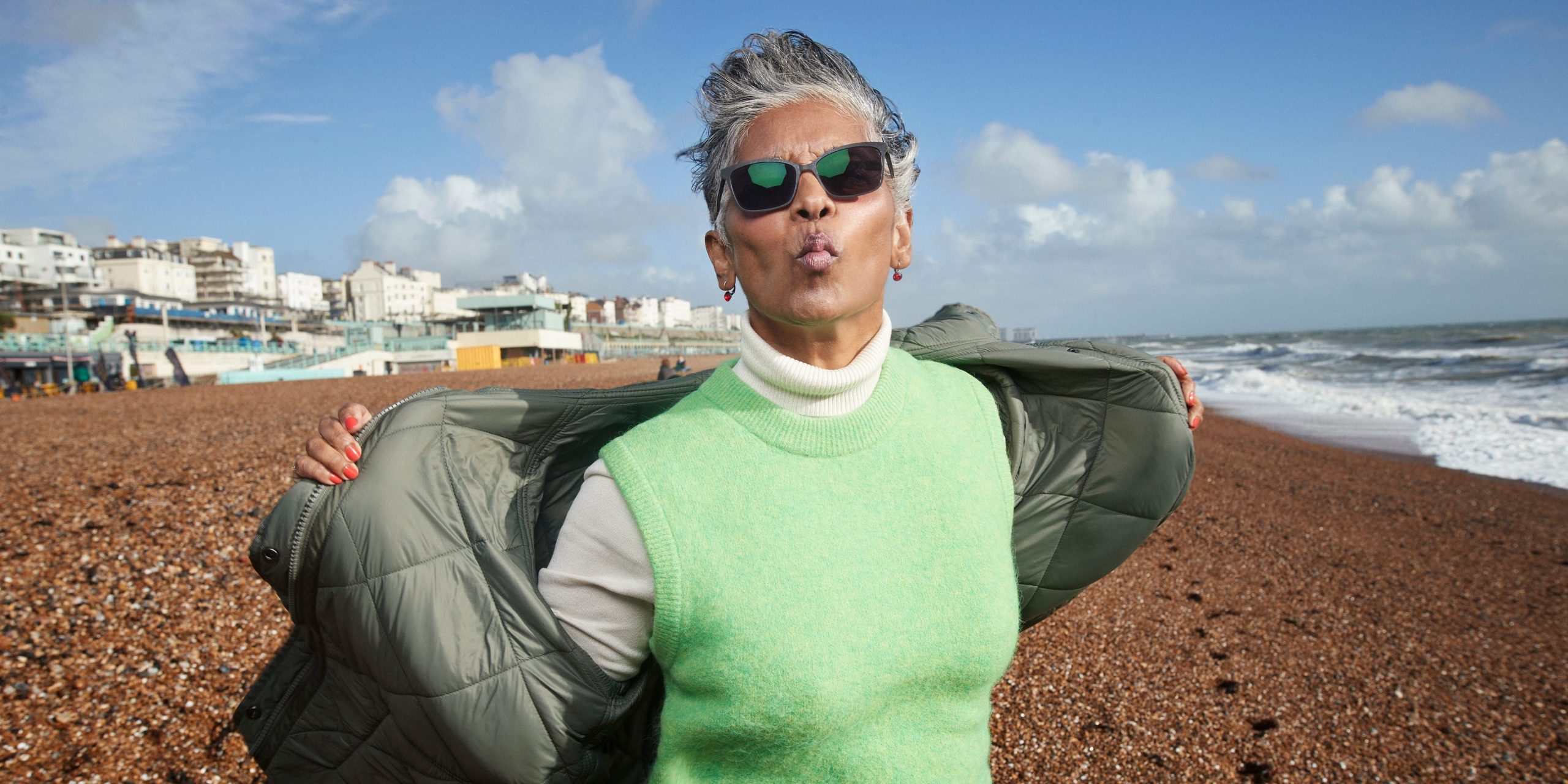 A senior woman puckers her lips while removing her jacket at a beach.