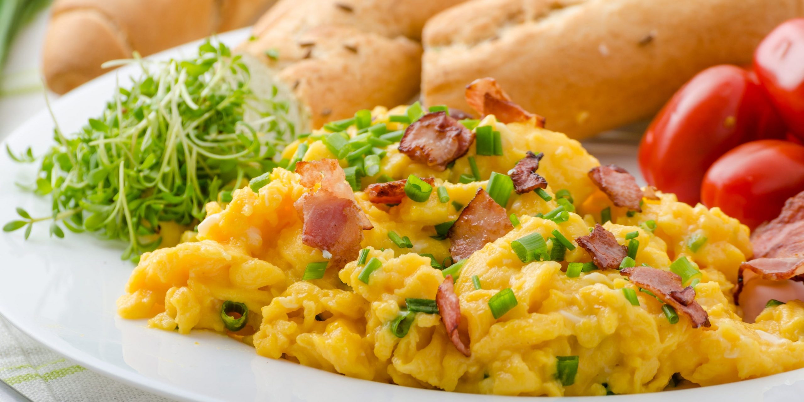 Scrambled eggs with bacon, chive and tomatoes, fresh juice and greens.