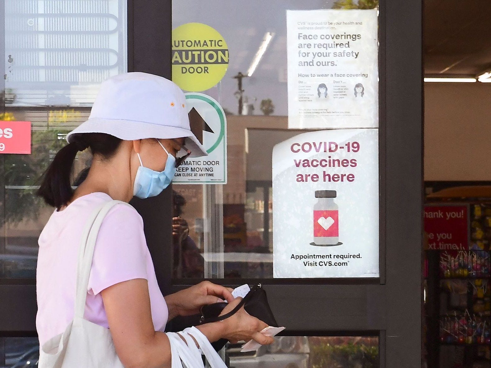 A woman enters a CVS drugstore in Monterey Park, California, with her mask on. a sign on the door advertises covid-19 vaccines are available.