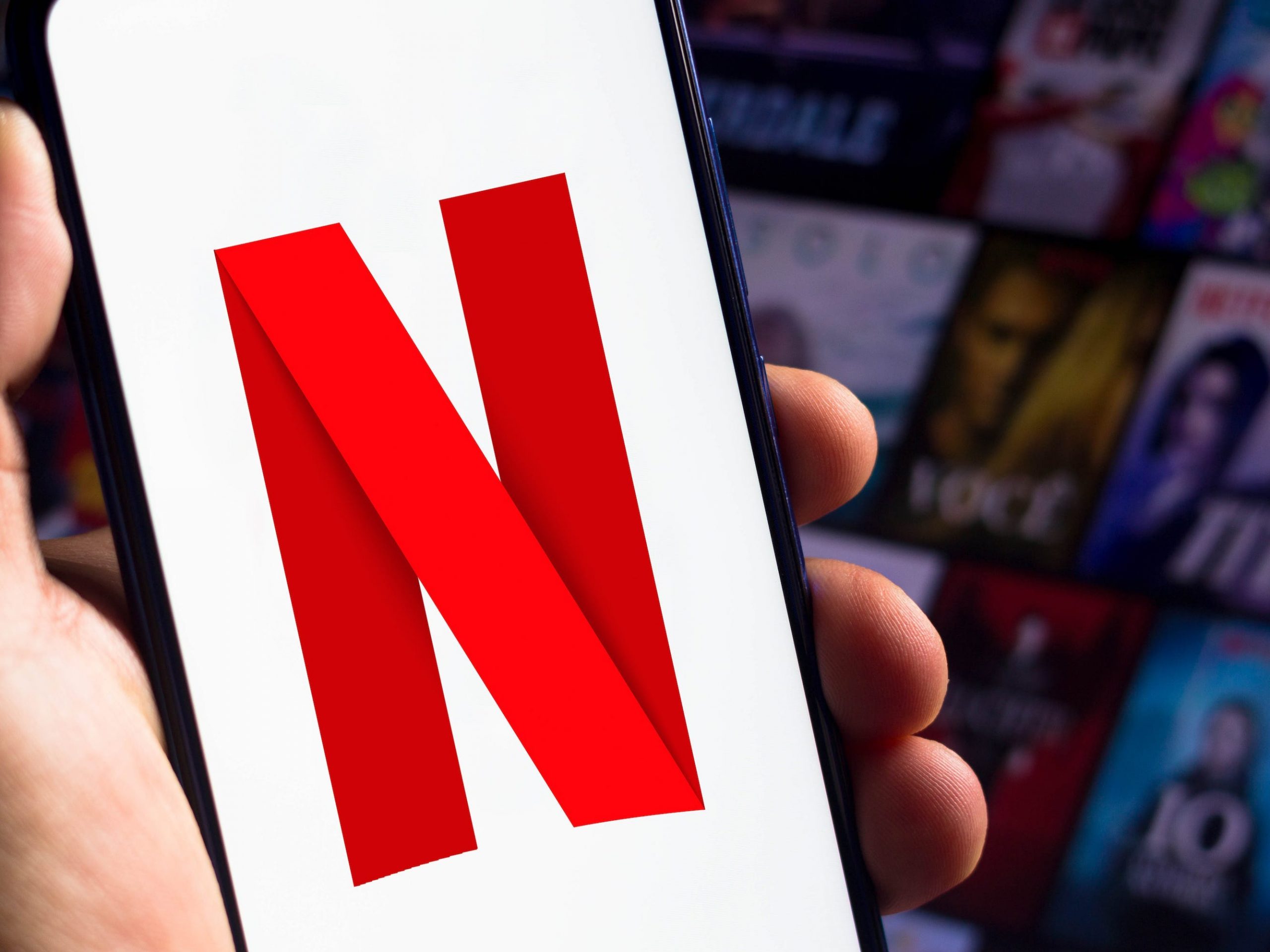 The Netflix logo displayed on a phone, with a selection of Netflix titles in the background.
