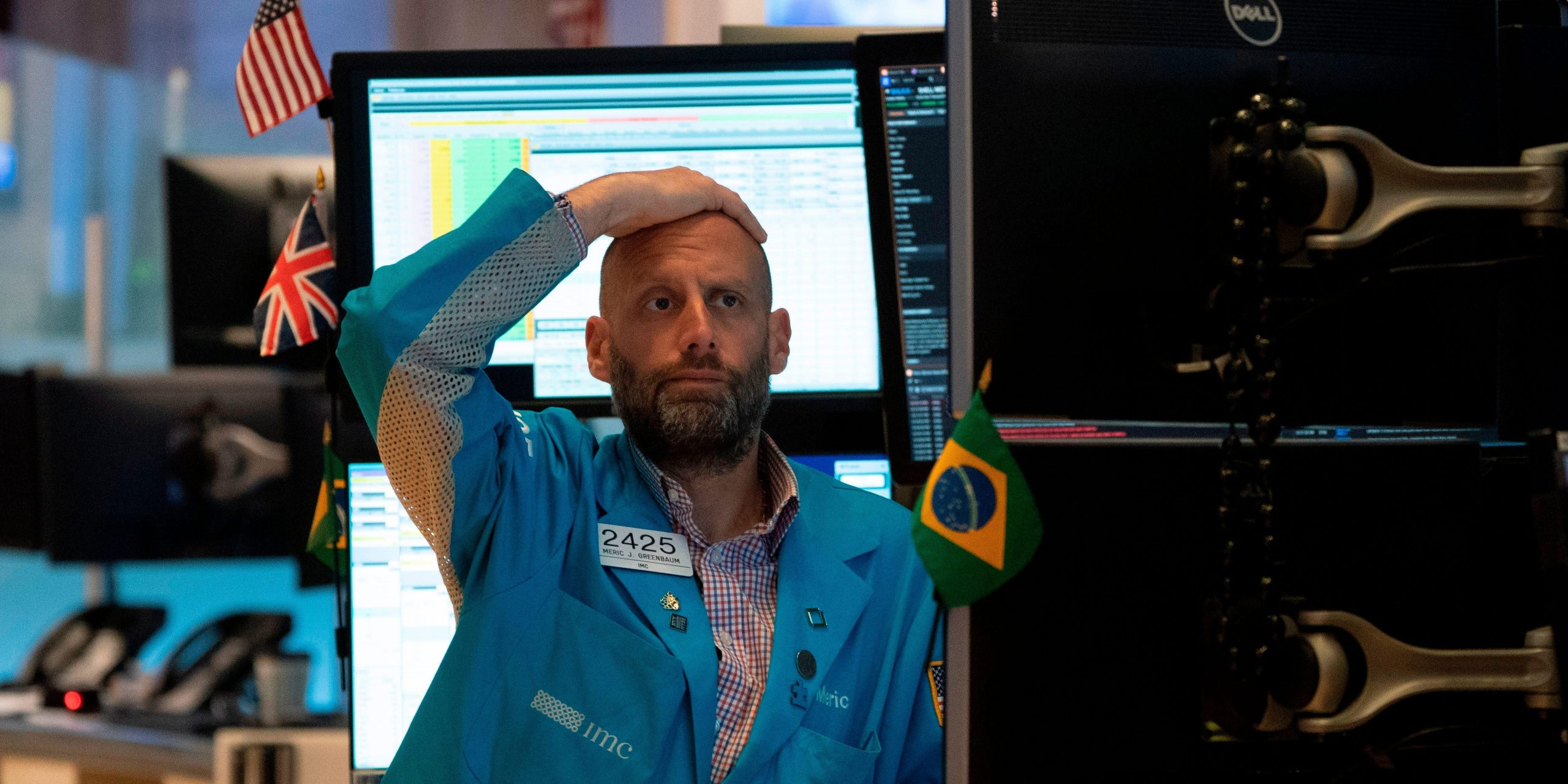 A trader looks distressed while staring at a computer screen, with his hand on his head.