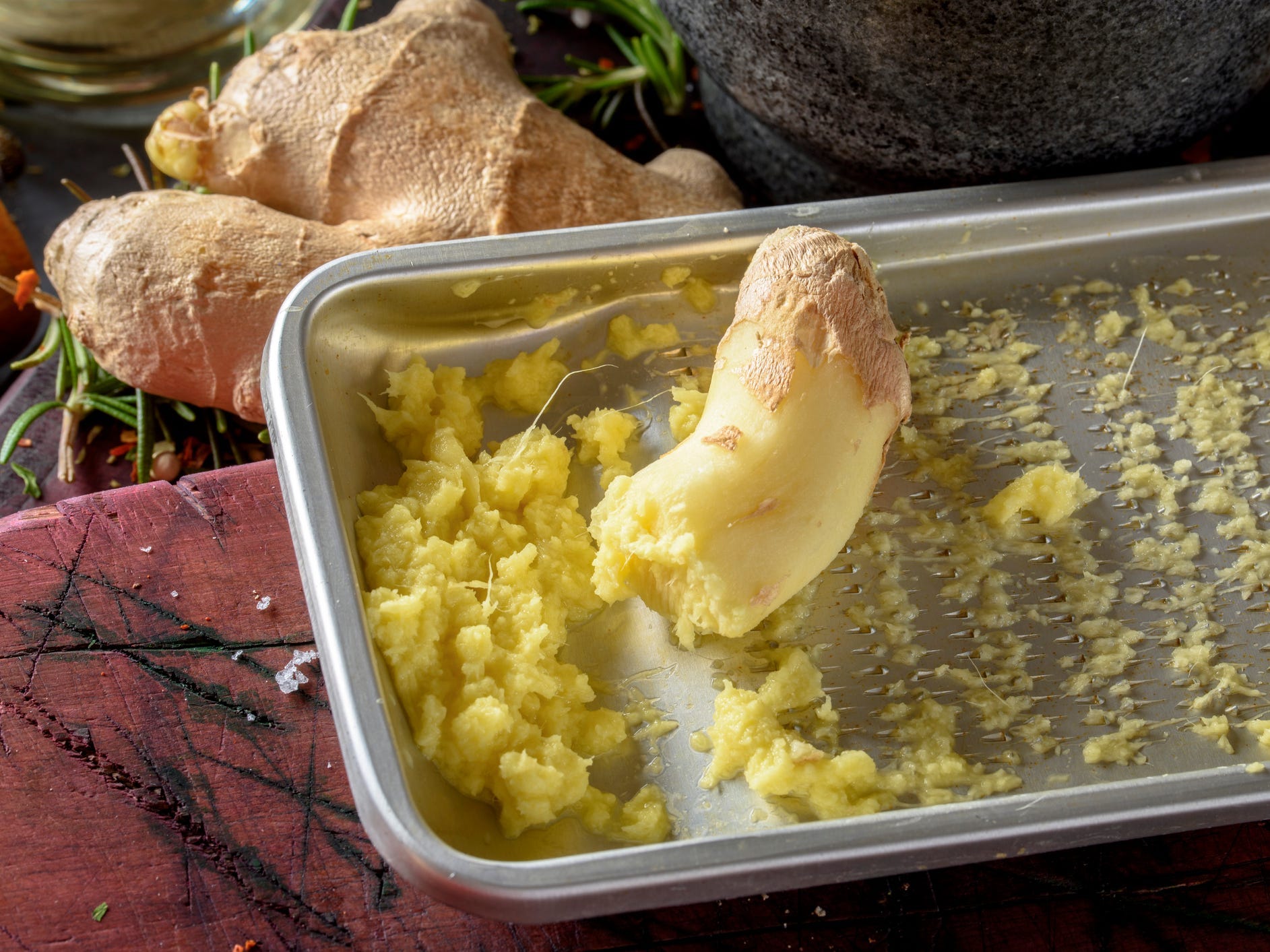 A nub of ginger sitting on top of a grater with a pile of grated ginger in it