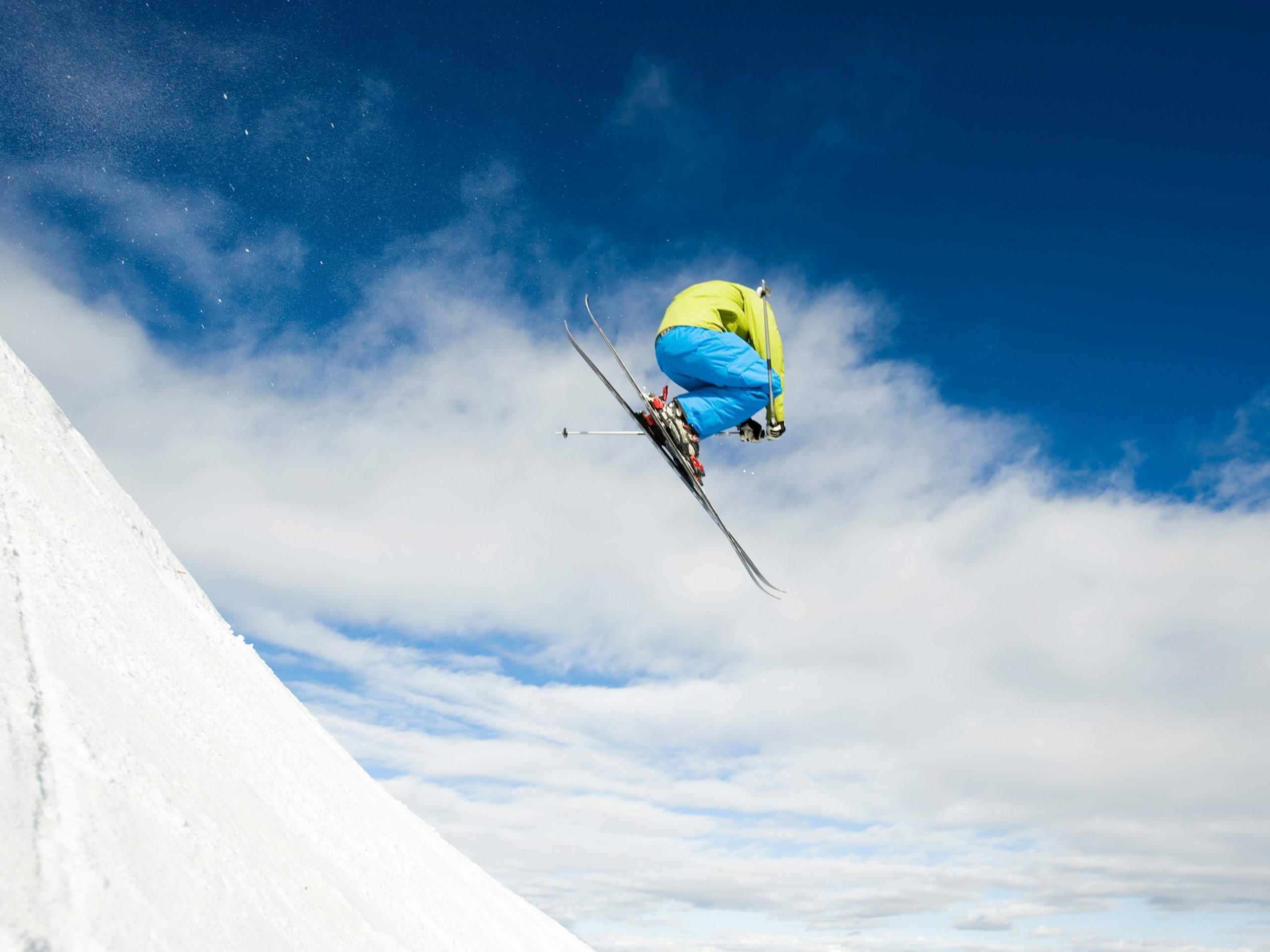 Male skier, wearing a light green jacket, bright blue snow pants, and red ski boots, in terrain park performing airborne maneuver. Snowmass Ski Area near Aspen, Colorado.