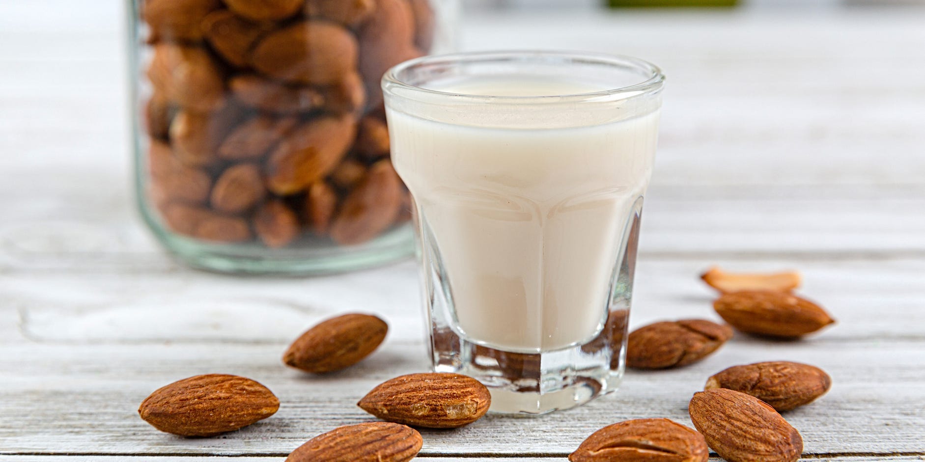 Almonds in a jar and a glass of almond milk surrounded by almonds.