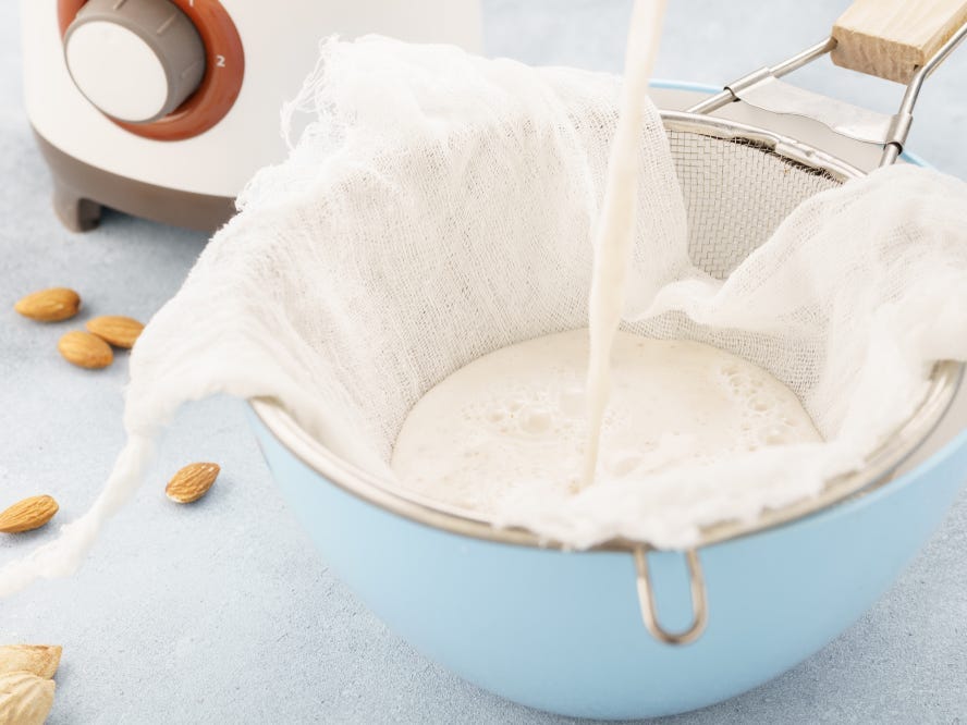 Homemade nut milk being poured through a strainer.