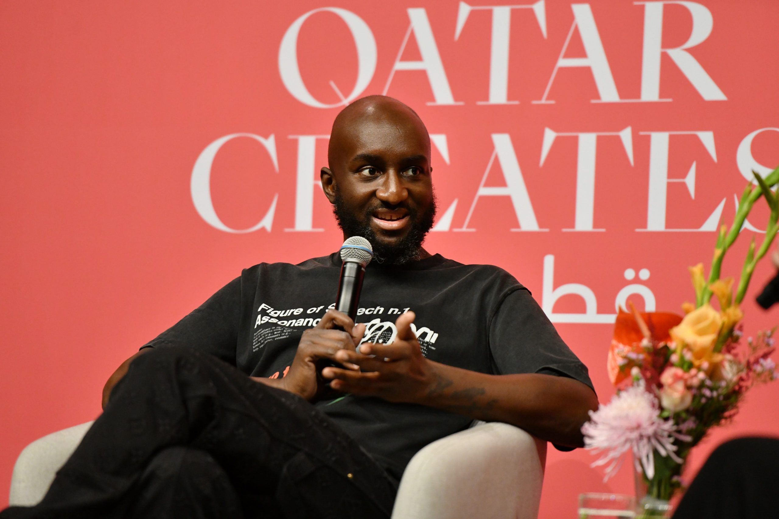 A man, seated, talks into a microphone as the words Qatar Creates appear behind him