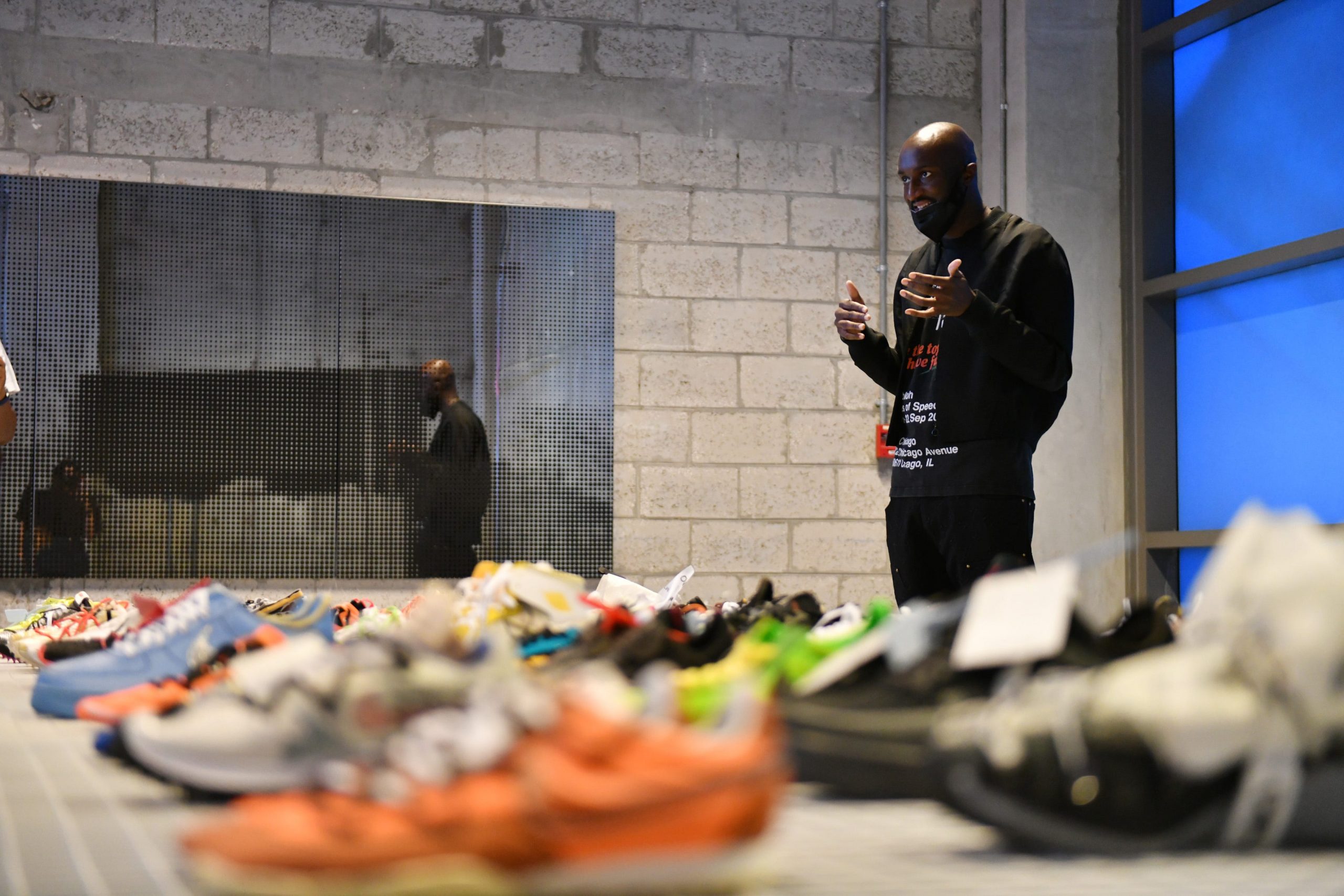 A man addresses an audience with a display of sneakers seen in the foreground.