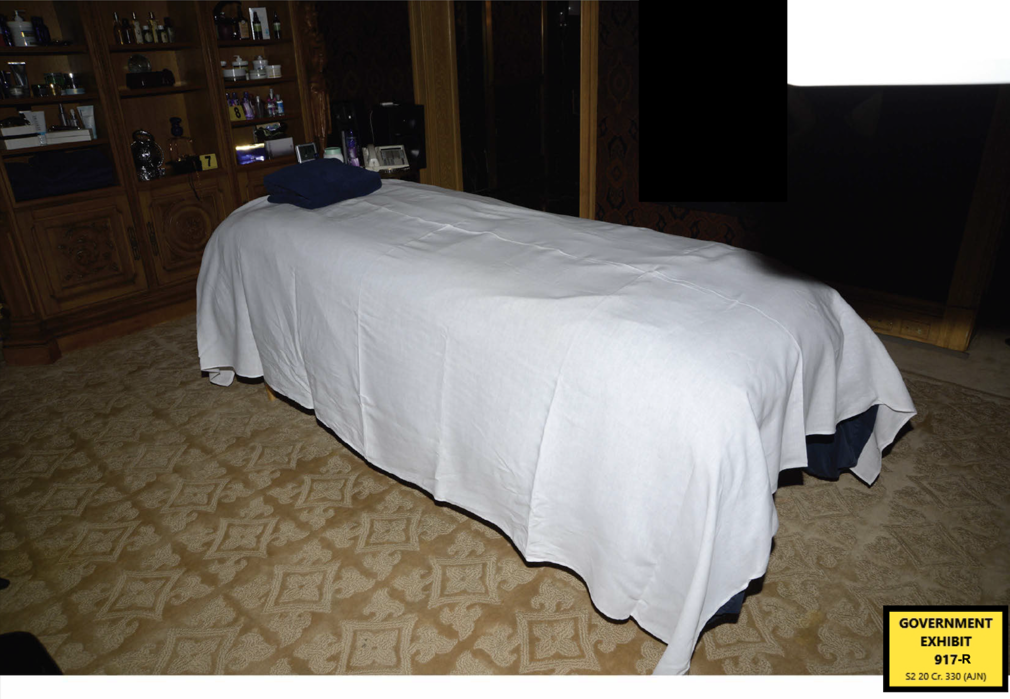 A photograph, labeled as a government exhibit, showing a massage table covered in a white cloth in a dark room