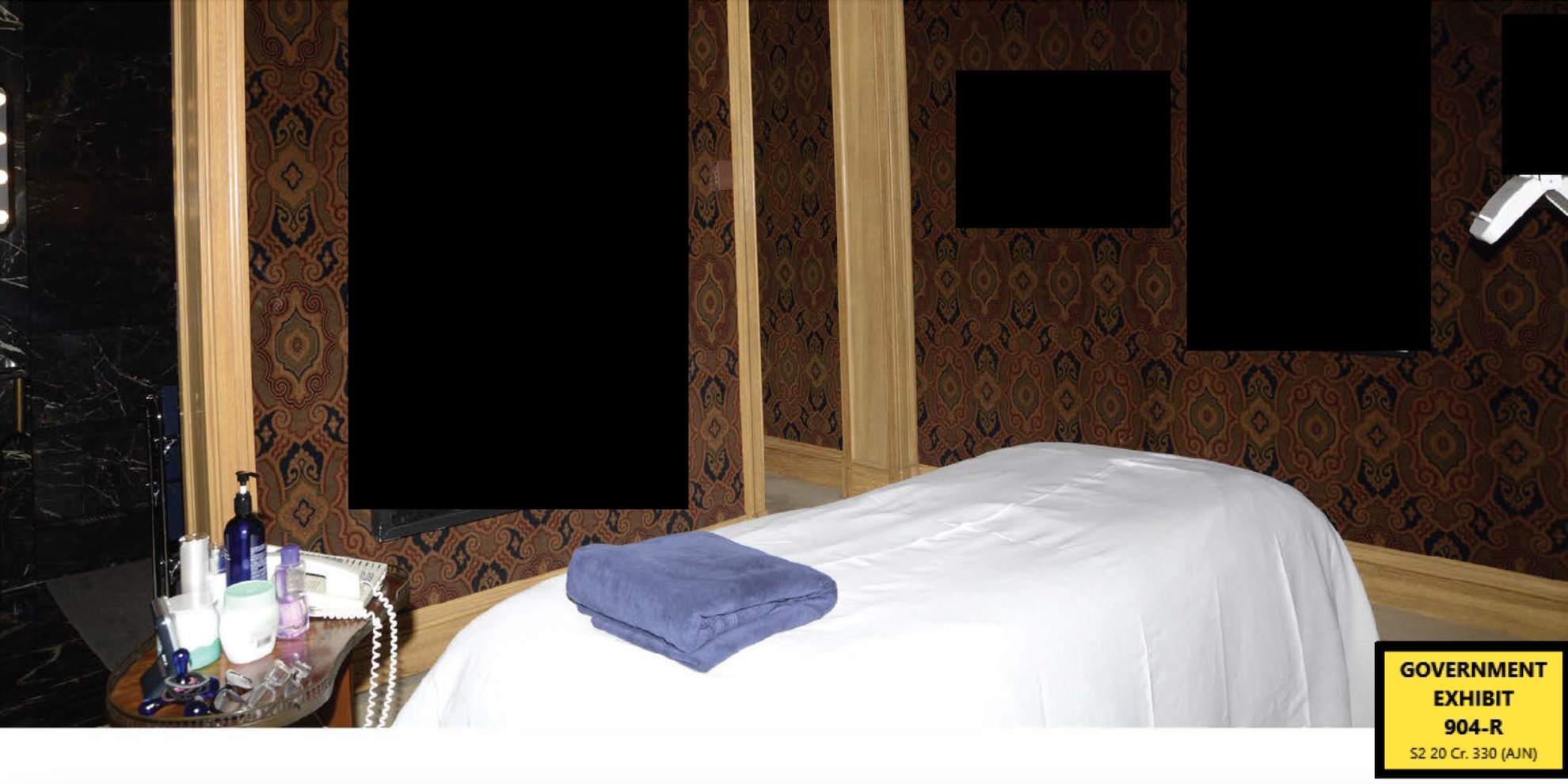 A photograph, labeled as a government exhibit, showing a massage table covered in a white cloth in a dark room