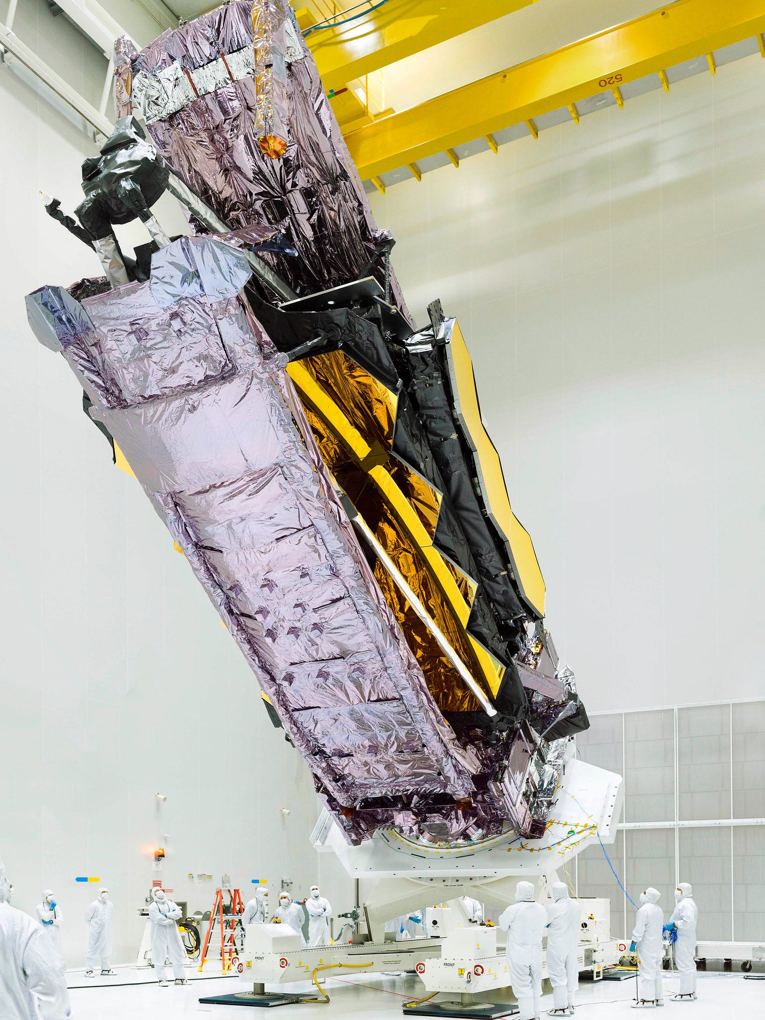 james webb space telescope lifted vertically enormous gold mirrors wrapped in purple foil inside white cleanroom