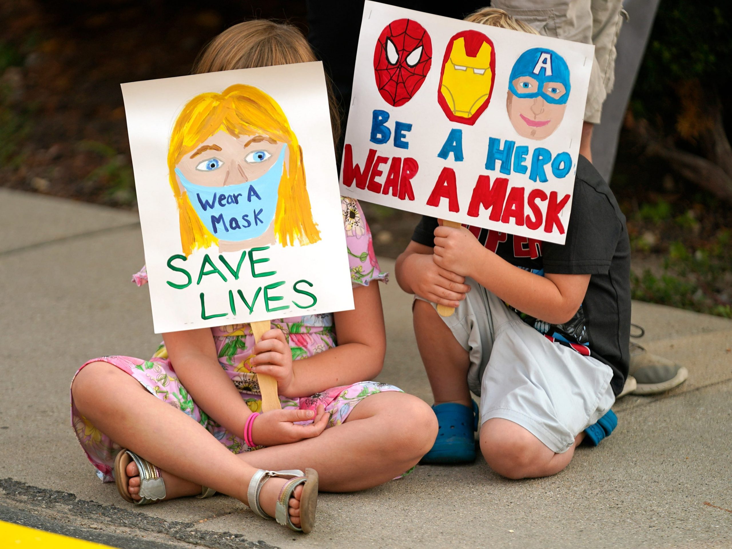 Two kids hold signs encouraging the wearing of masks in the classroom.