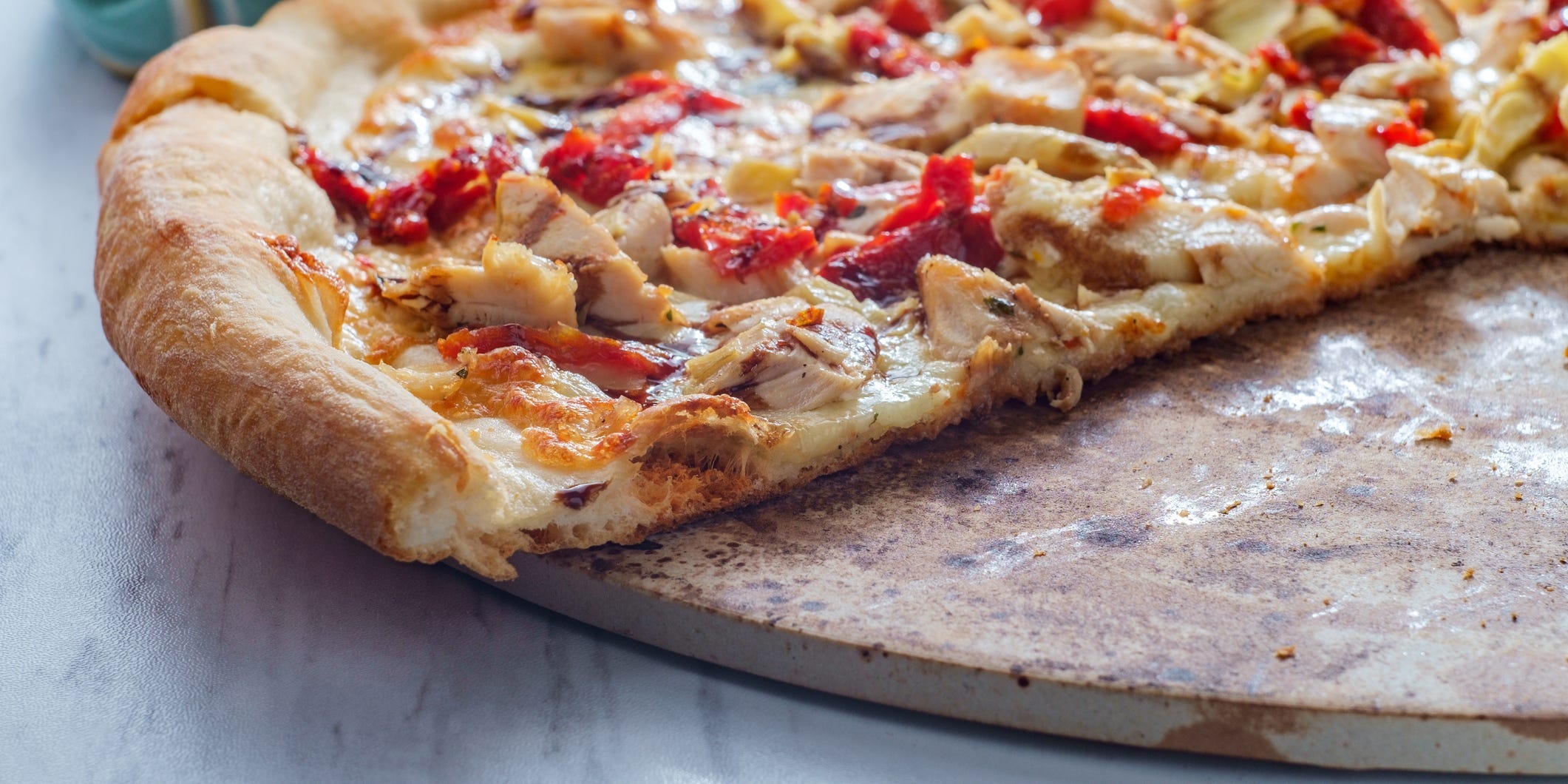 A homemade pizza topped with chicken and peppers with slices removed revealing a pizza stone underneath