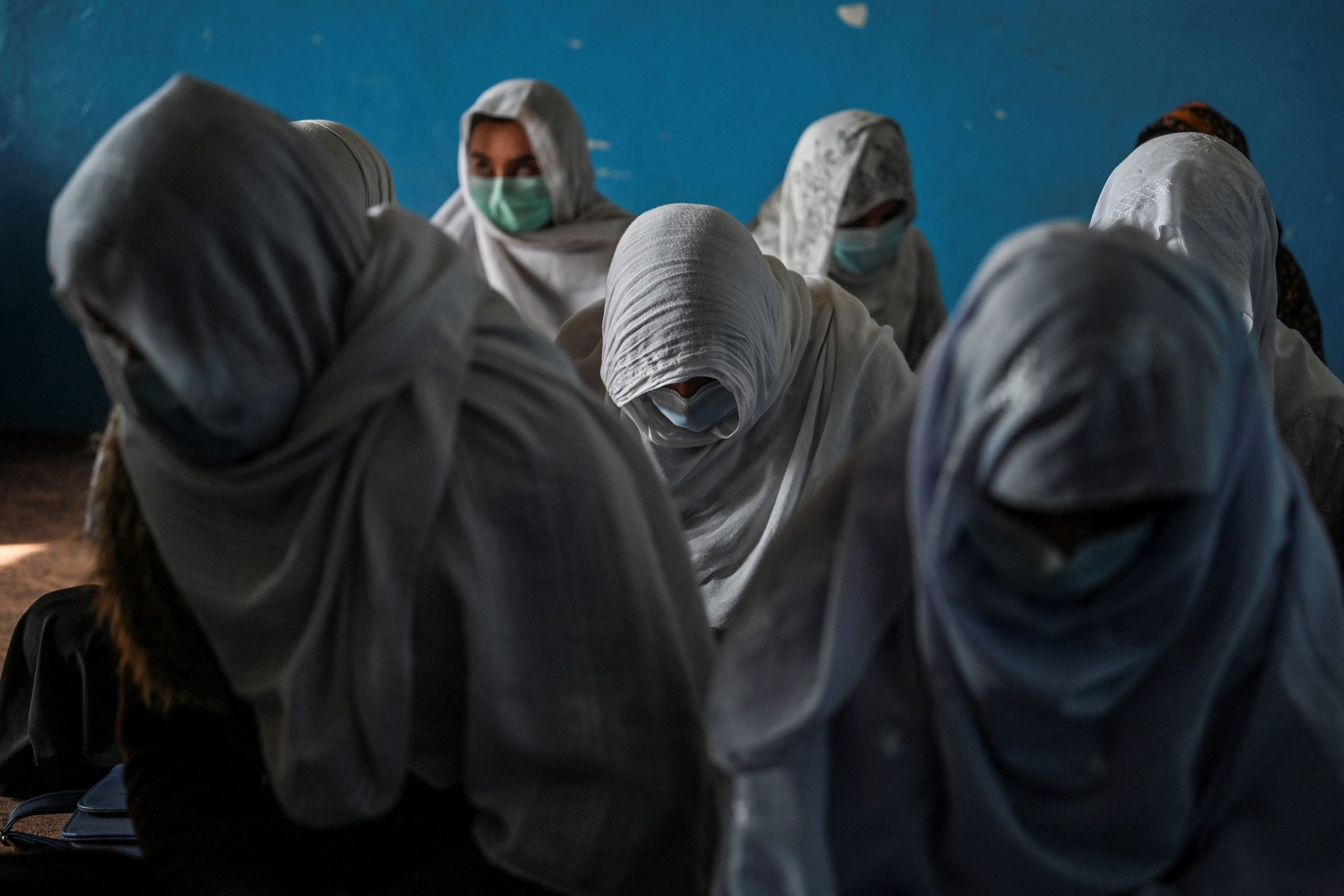 Afghan women sit in a classroom while garbed in shawls covering their heads and faces.