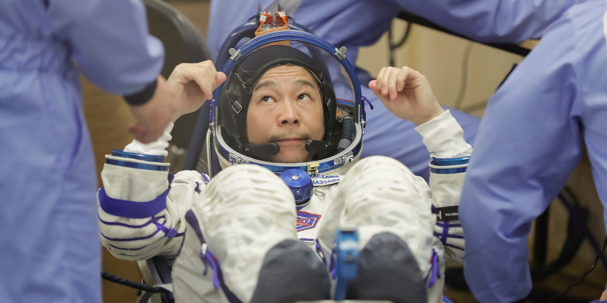 Yusaku Maezawa in a space suit, looking at people as they check its fit