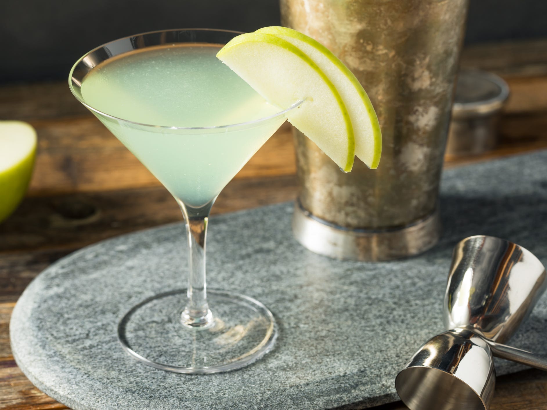 An appletini garnished with two green apple slices surrounded by barware