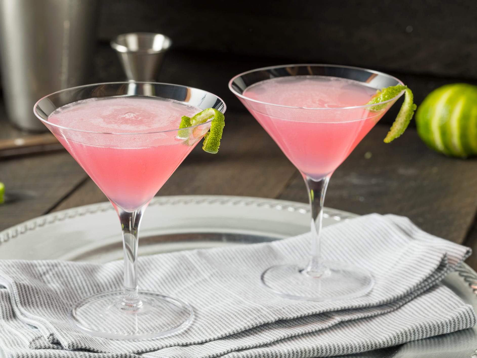 Two cosmopolitan cocktails garnished with lime twists on a serving tray