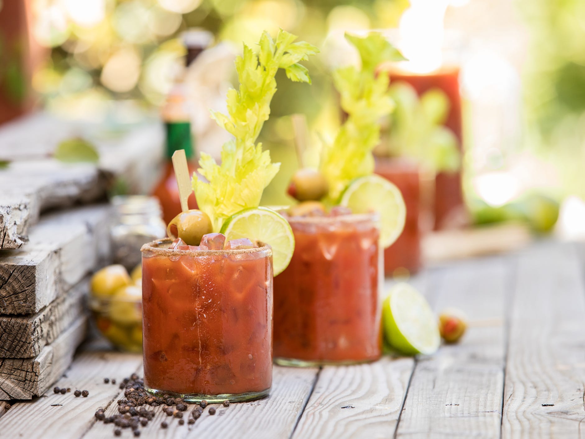 Two bloody mary cocktails garnished with lime wheels and celery sticks on an outdoor wooden bar