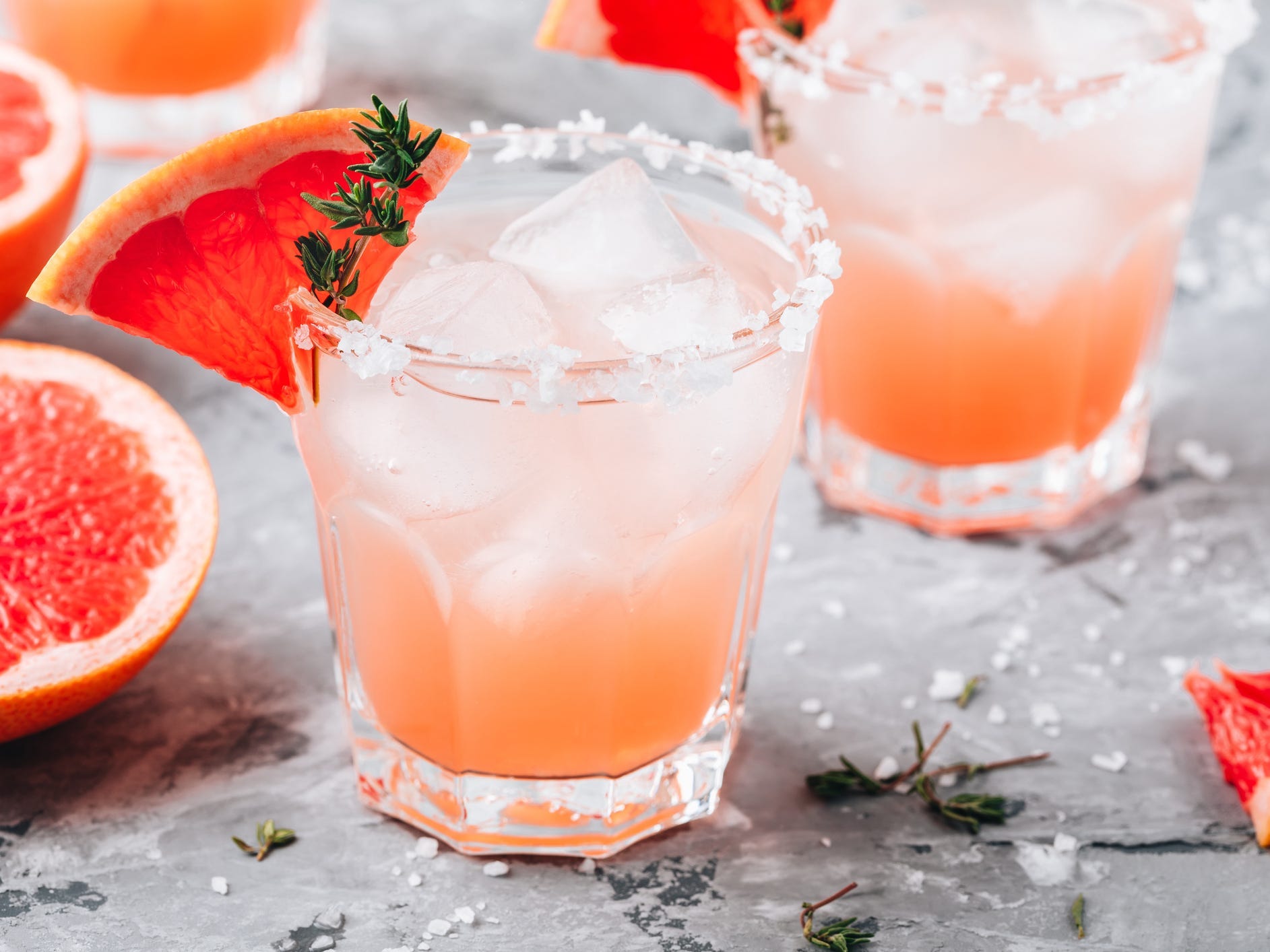 Two salty dog cocktails garnished with grapefruit slices and herbs